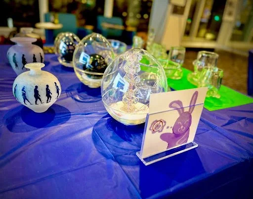 various glass artifacts presented at a convention, witha small piece of paper displaying a hard painted bunny.