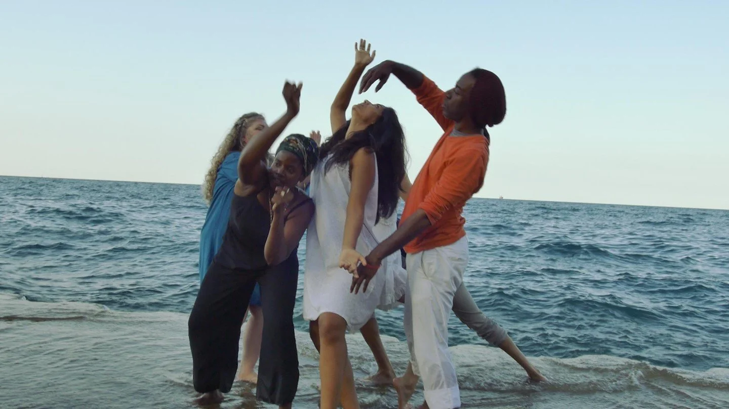 Film still of group of four people dance interpretively alongside the waters of Lake Michigan.