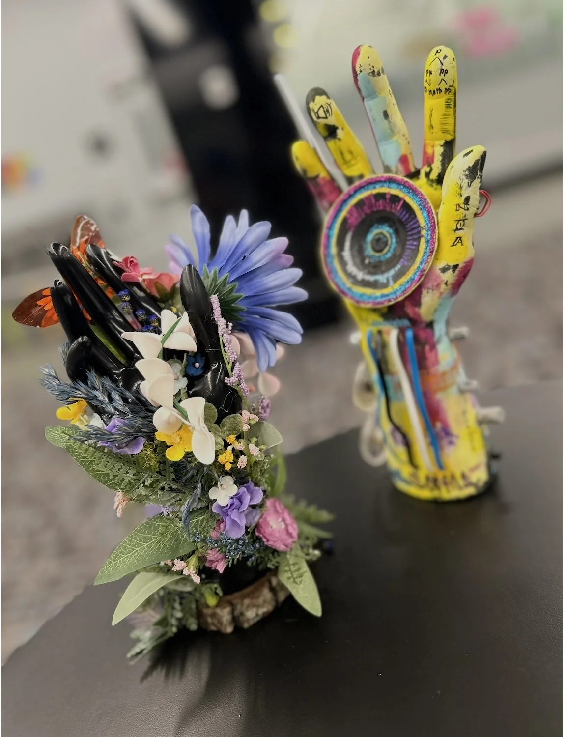 Two sculptures depict brightly coloured hands. One is covered in 3-D flowers.  The other has a round circle in its palm.