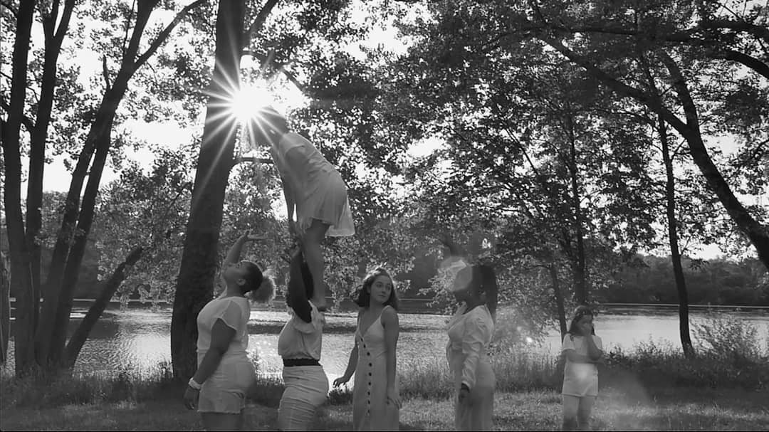 Film still of femme figures dressed in white, engaged in a ritual near the water