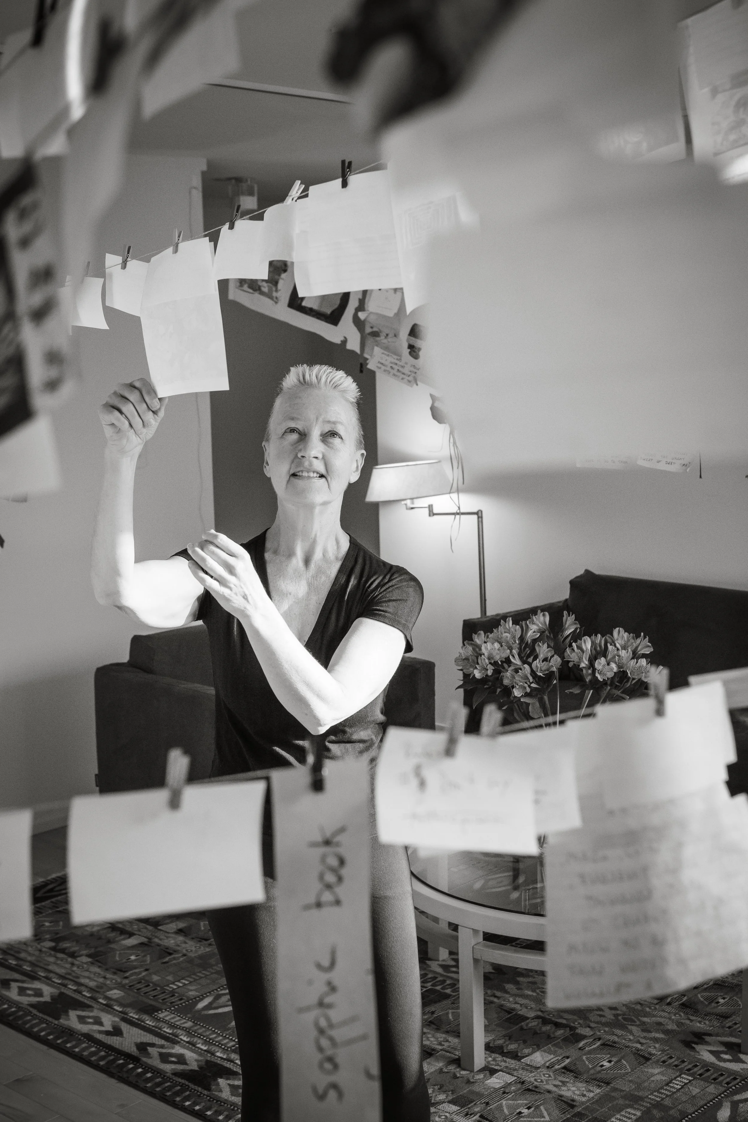 The author (Lynne Huffer) hangs fragments of collage and writing from clothespins on strings stretching across the room.