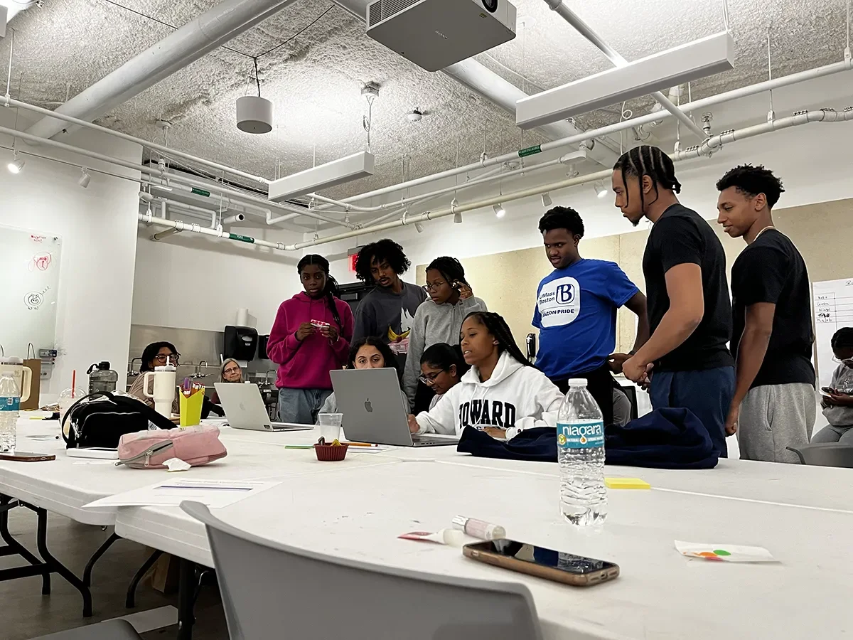 Creative AI & Design “prompt battle” at Lesley University (a group of students gather around a laptop in a college classroom)