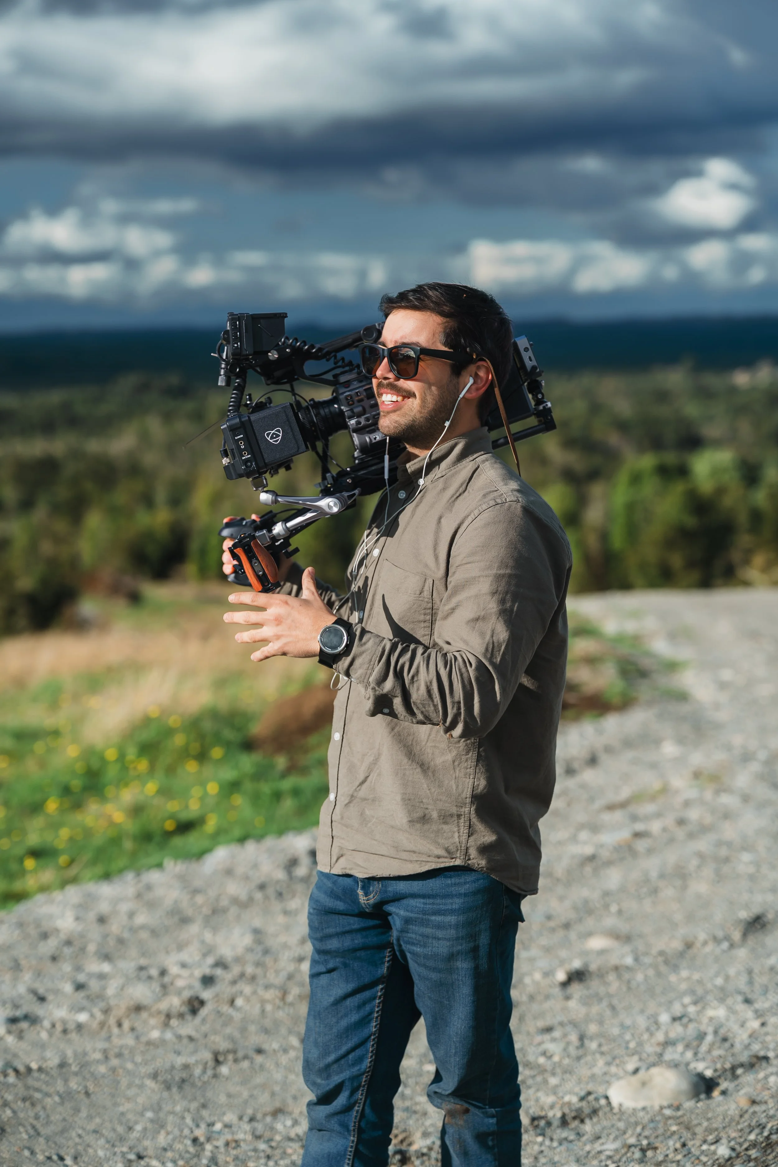 Hombre con equipo de filmación en un campo ao aire libre con cielo nublado.