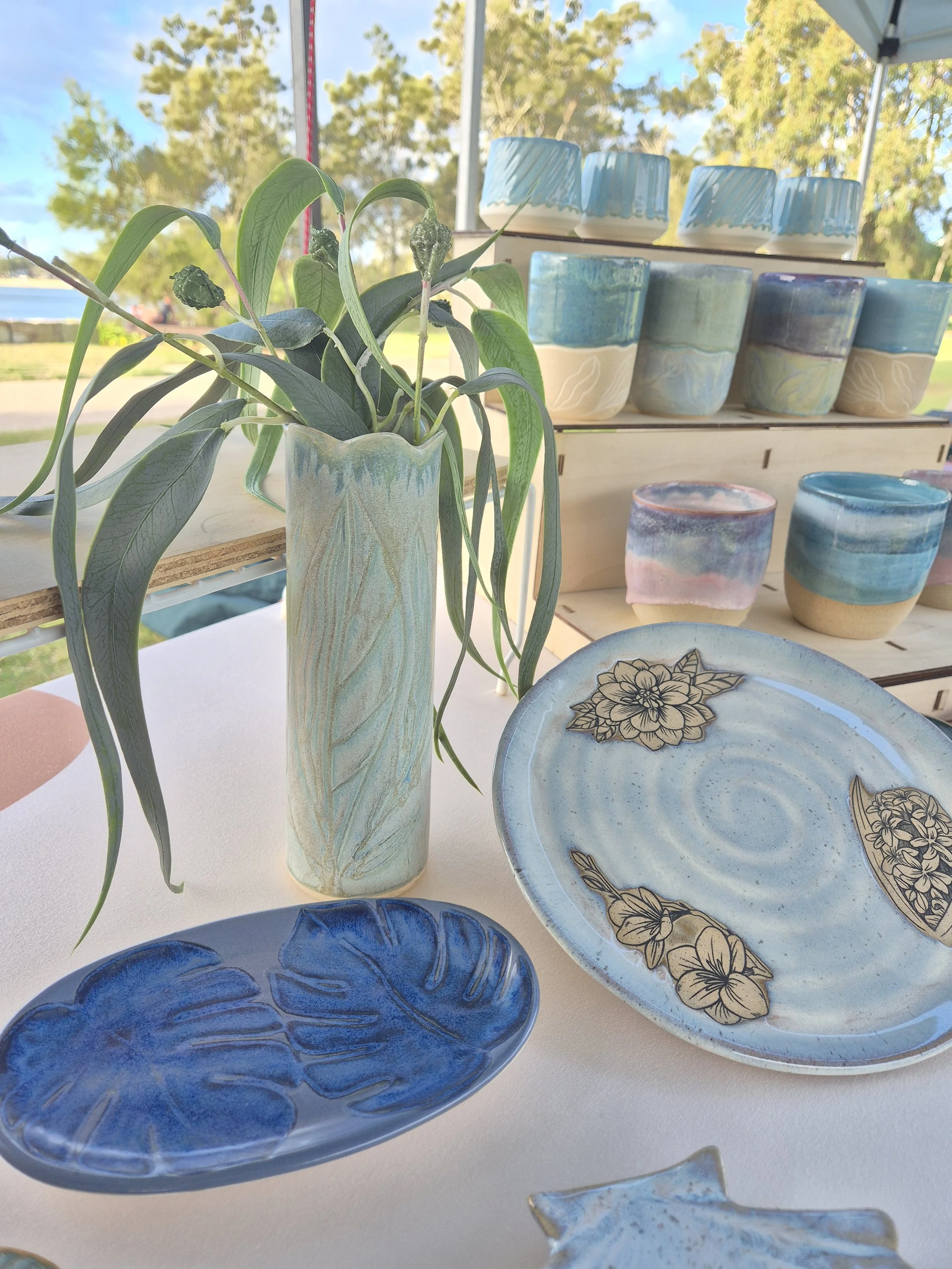 A collection of handcrafted ceramic plates, a vase, and cups arranged on a table in a park.