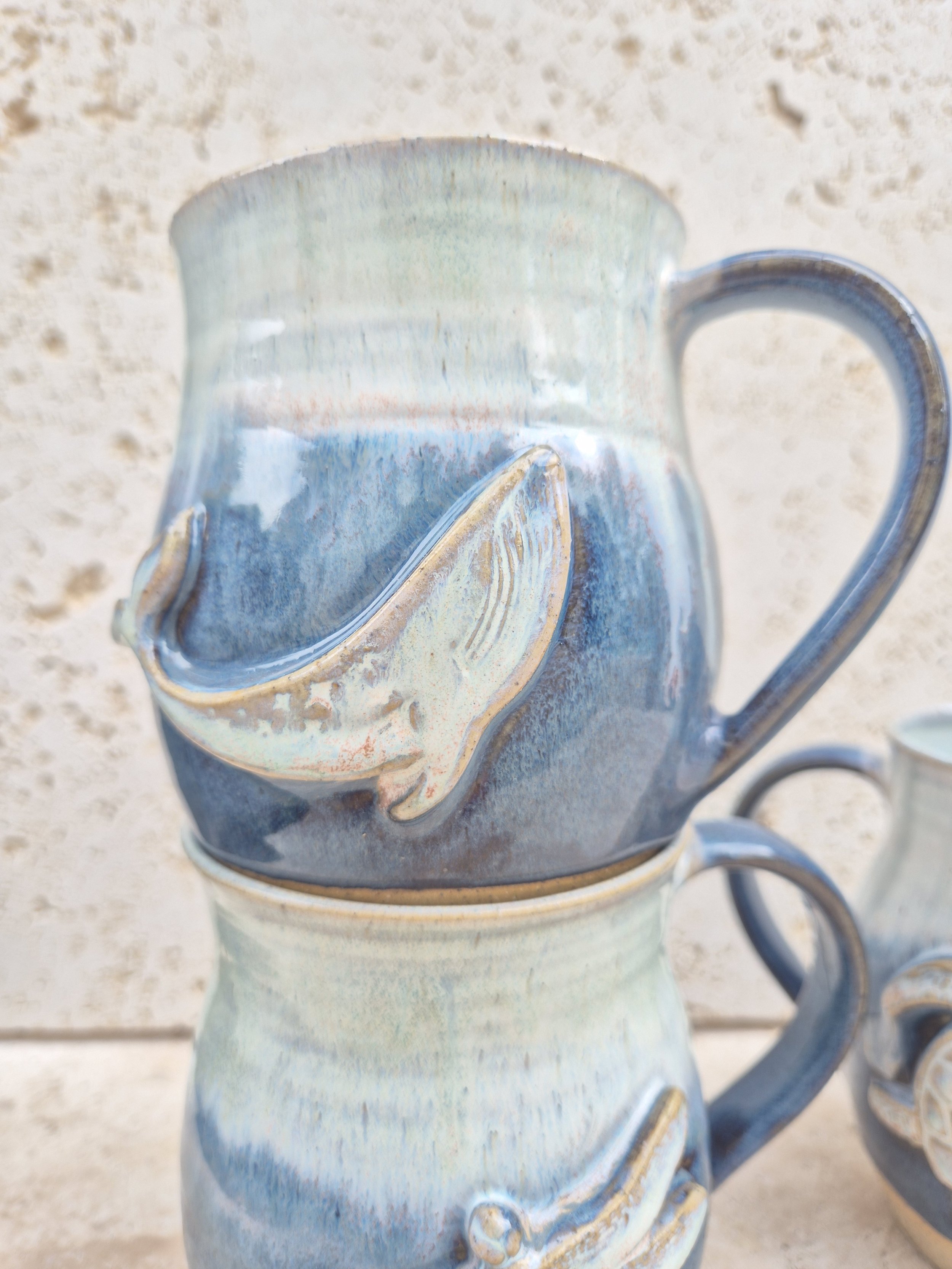 A ceramic mug with a blue glaze sitting on top of another matching mug, both placed on a wooden surface.