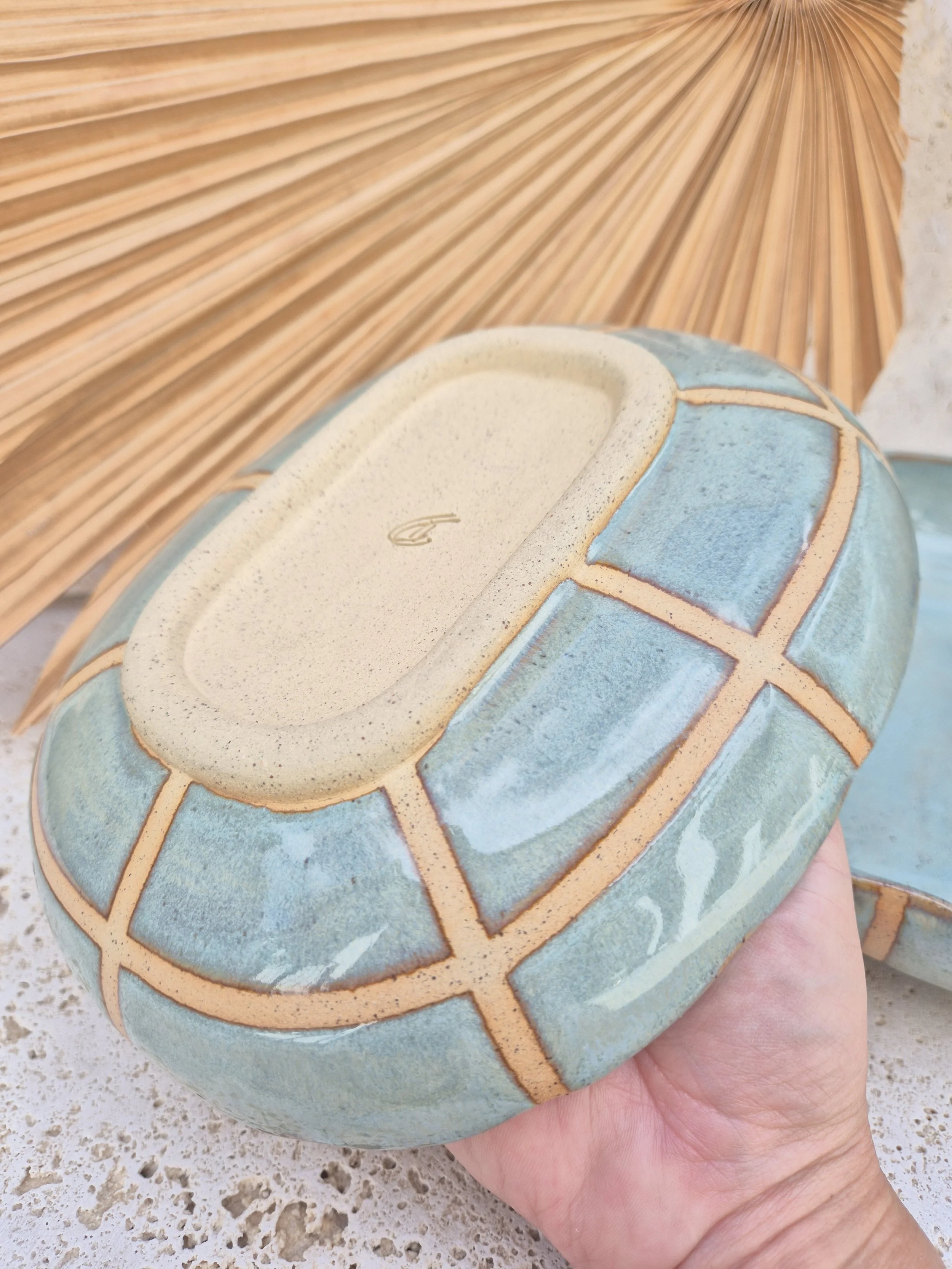 Underside view of a handcrafted ceramic dish featuring a blue checked glaze pattern.