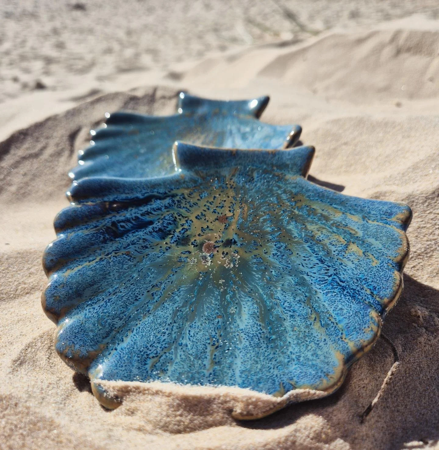 A blue ceramic leaf-shaped dish on sandy ground with the ocean in the background.