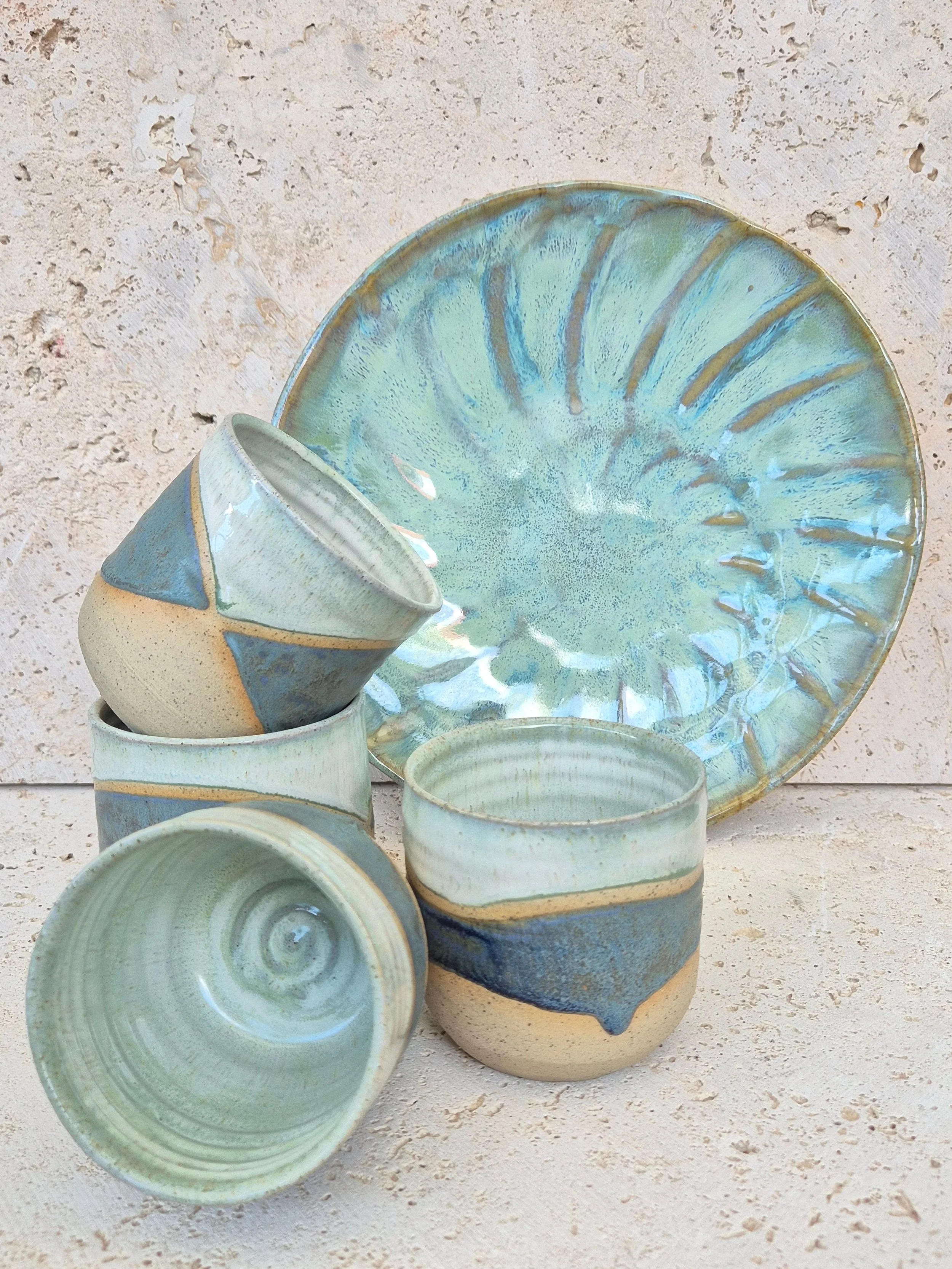 A set of handcrafted ceramic cups and a plate featuring varying tones of blue glaze with subtle patterned detailing.