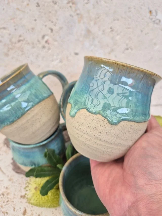 Handmade ceramic mugs finished in a smooth blue glaze, arranged to highlight their natural variations in tone, texture, and form under soft lighting.
