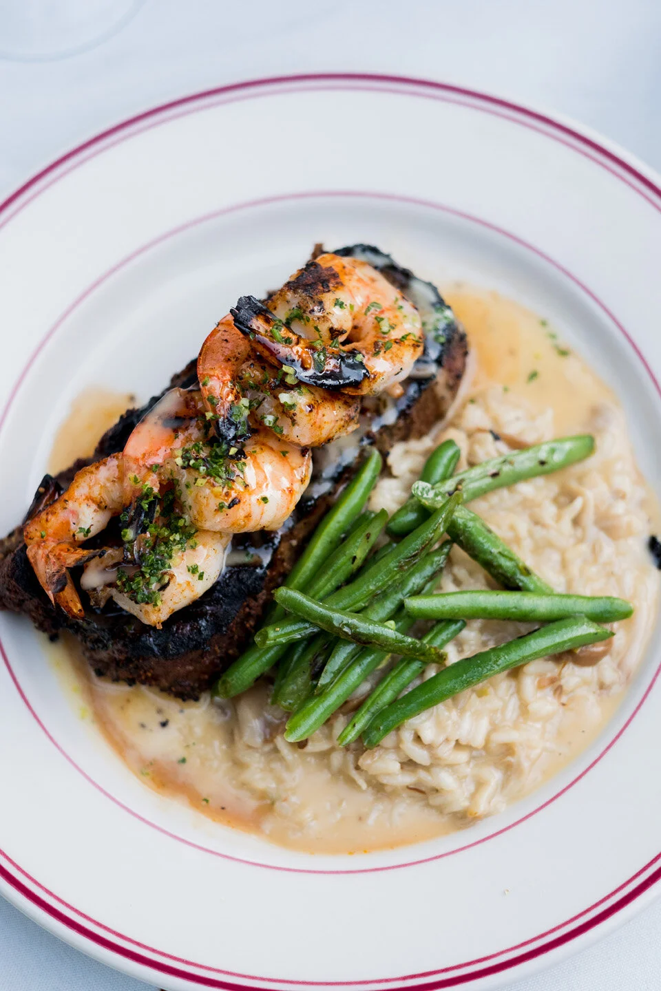 Shrimp and grits with green beans on a white plate with red trim.