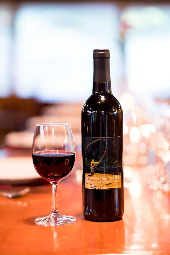 A bottle of red wine and a glass filled with red wine on a wooden table.