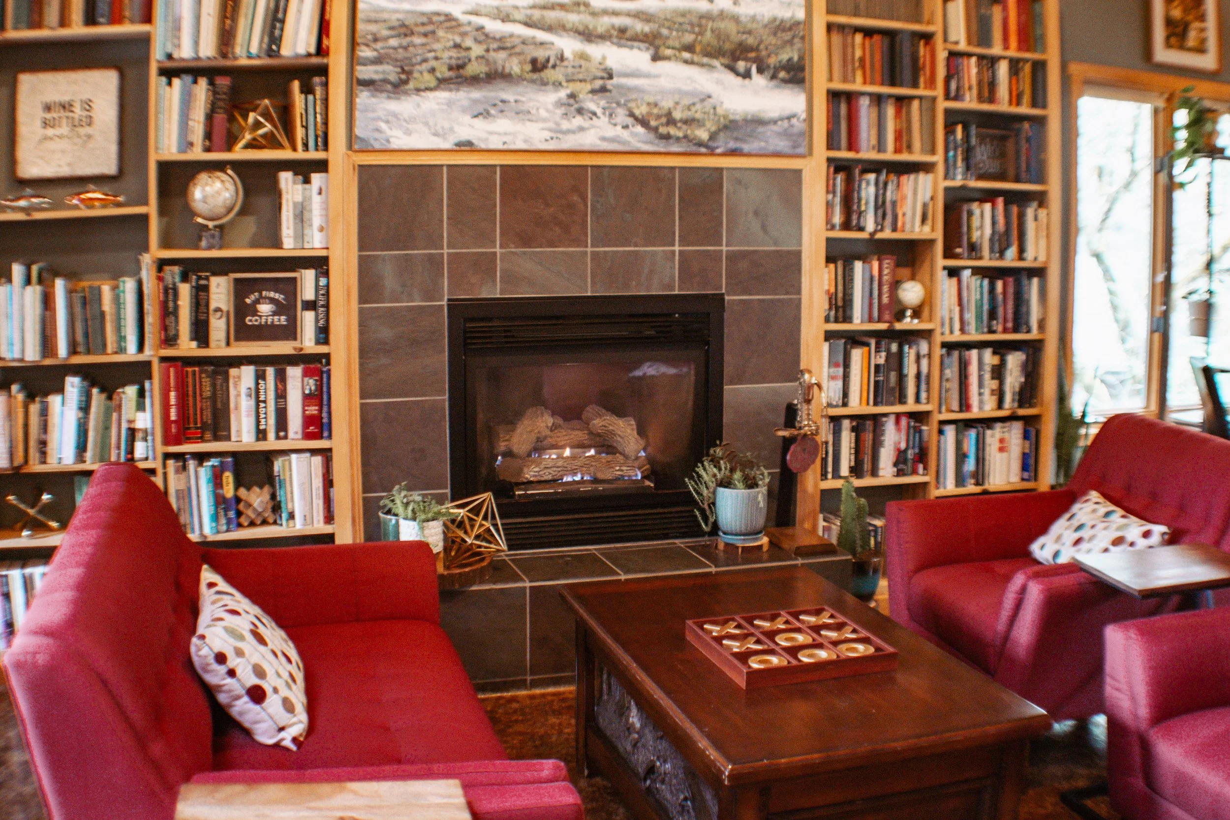 Living room with a fireplace, surrounded by bookshelves filled with books and decorative items, with red sofas and a wooden coffee table.
