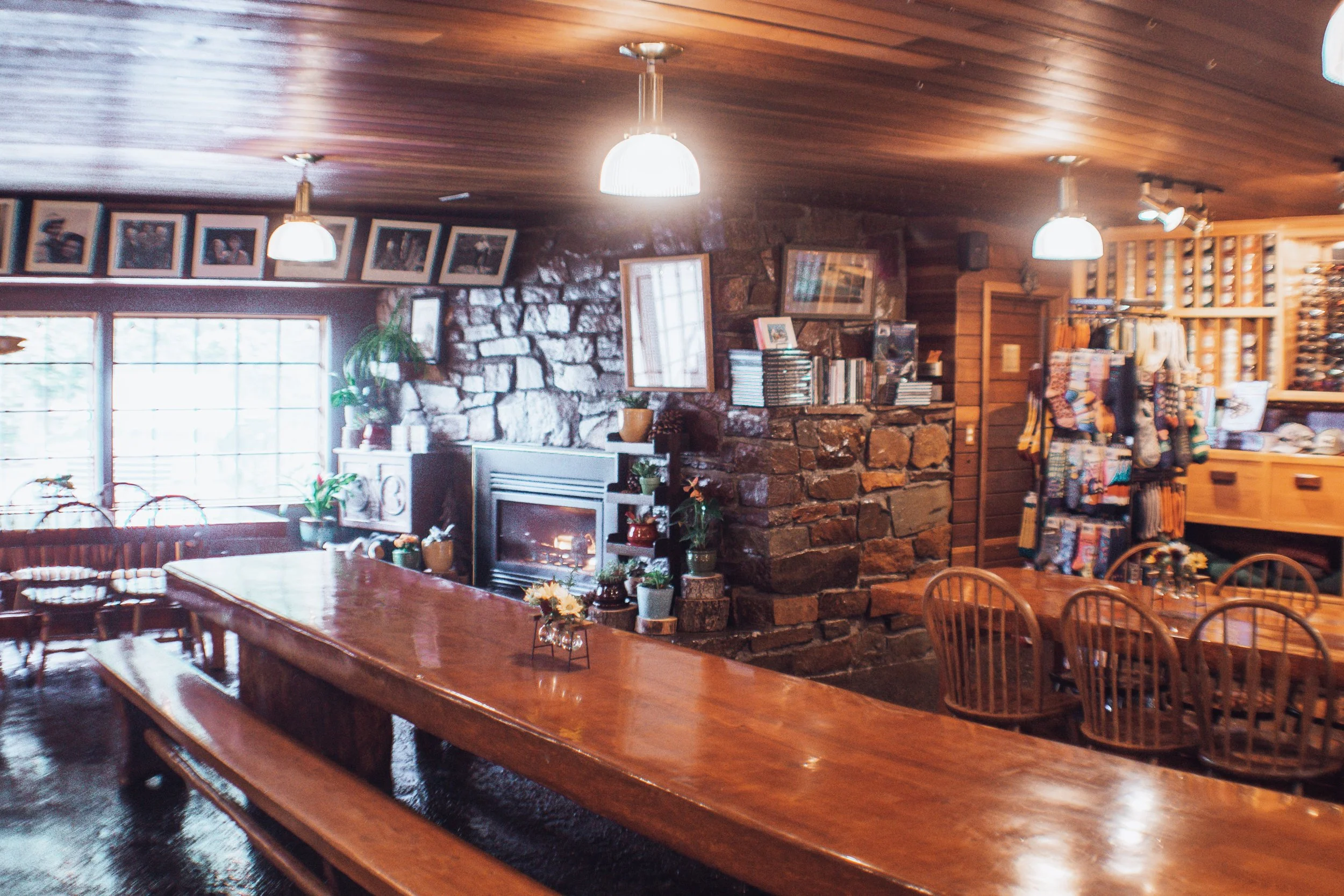 Cozy wooden interior with a large table, chairs, a stone fireplace, and shelves with books and decorative items.