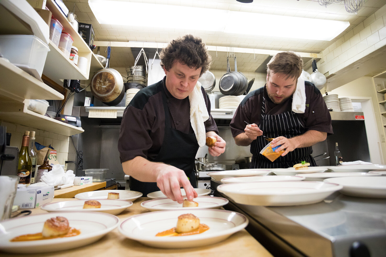 Two chefs preparing plated dishes in a restaurant kitchen.