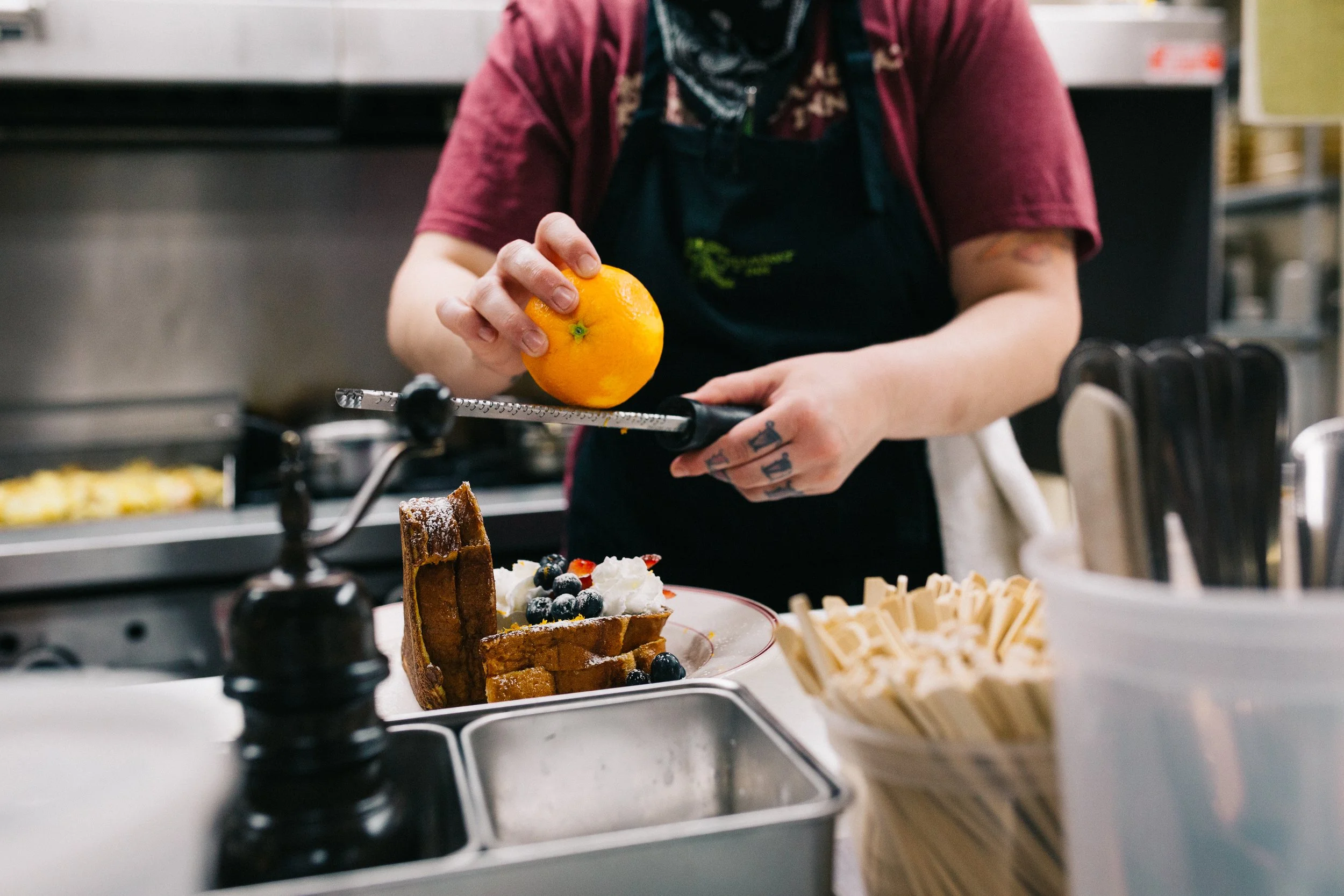 Person garnishing a waffle with blueberries and whipped cream in a kitchen.