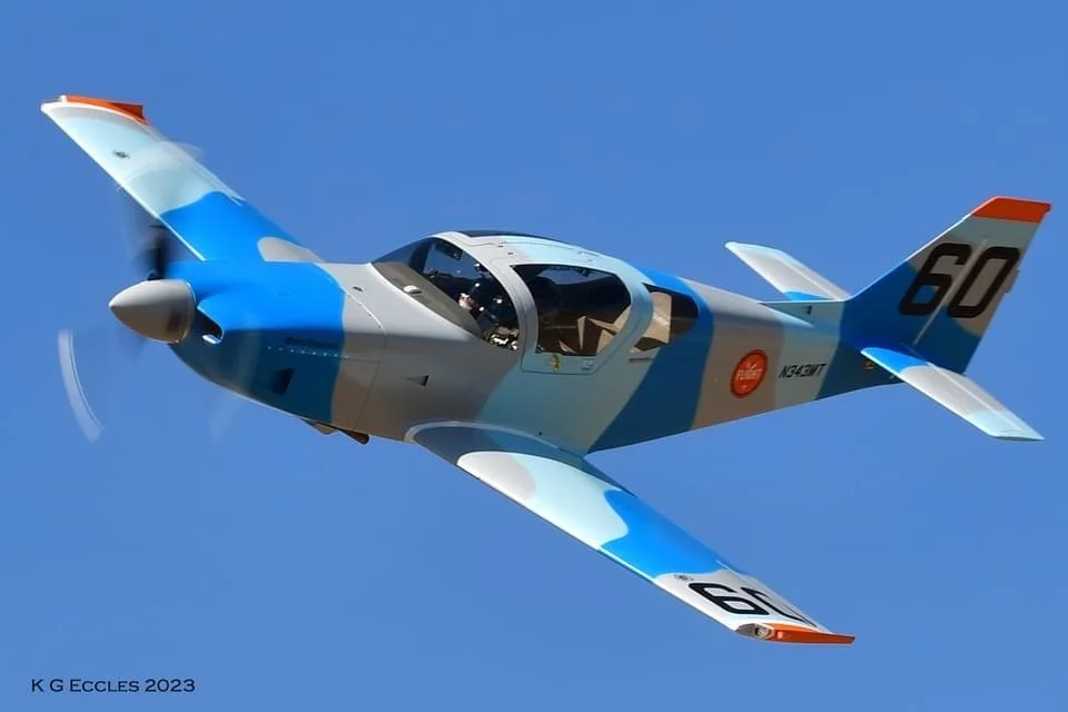 A modern fighter jet with a blue and gray camouflage pattern flying in a clear blue sky.