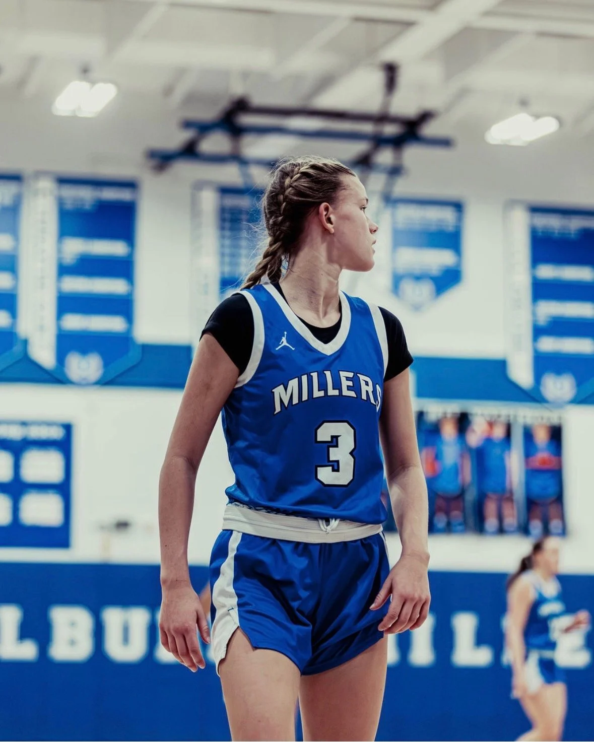 A female basketball player wearing a blue jersey with the number 3 and the word 'MILLERS' on it, standing on a basketball court.