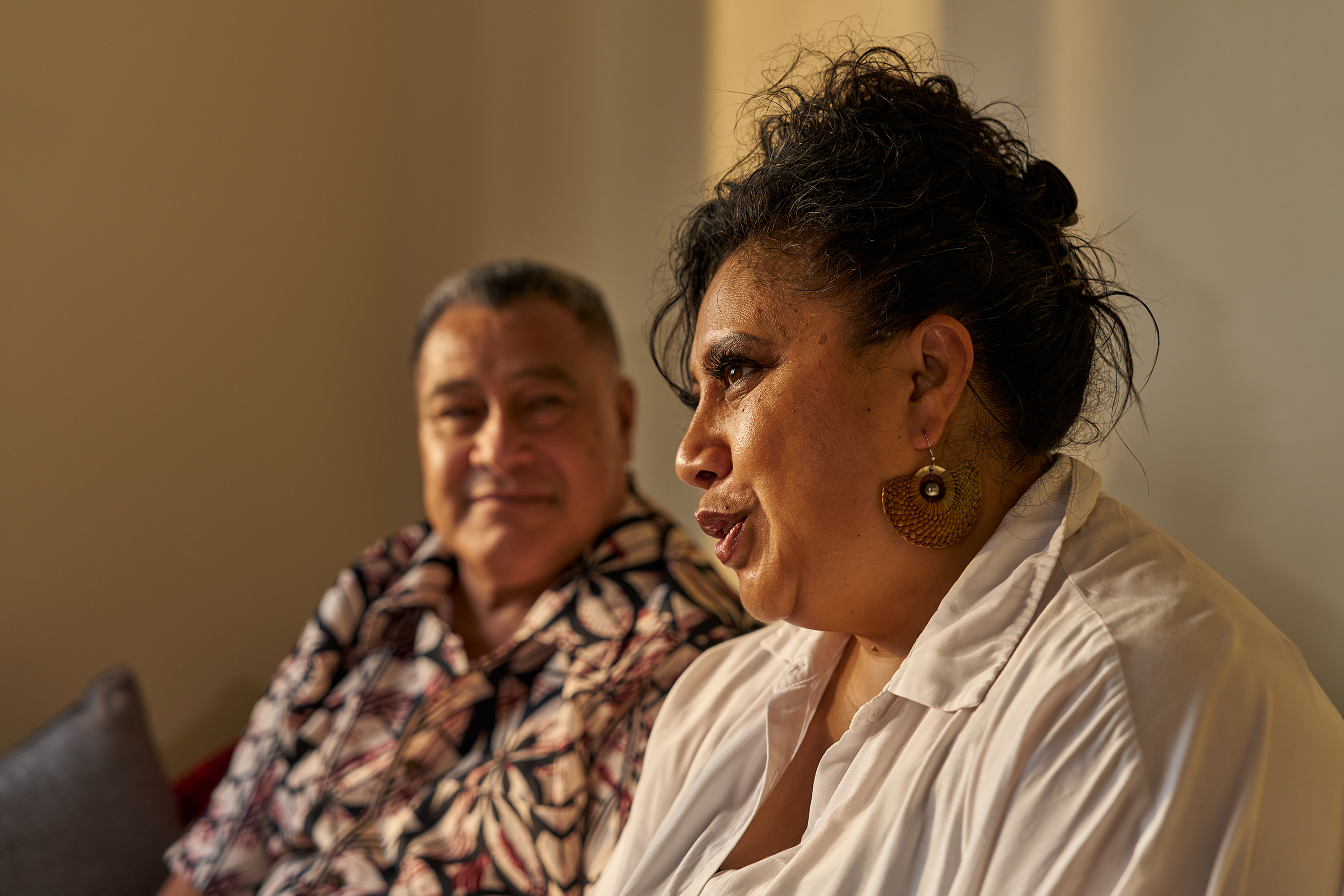 Two women sitting together, one in a patterned blouse and the other in a white shirt, engaged in conversation at an indoor event.