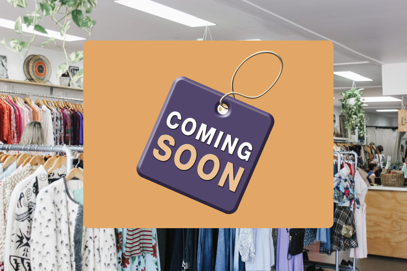 Sign that says 'COMING SOON' hanging in a thrift store with clothing racks and shoppers in the background.
