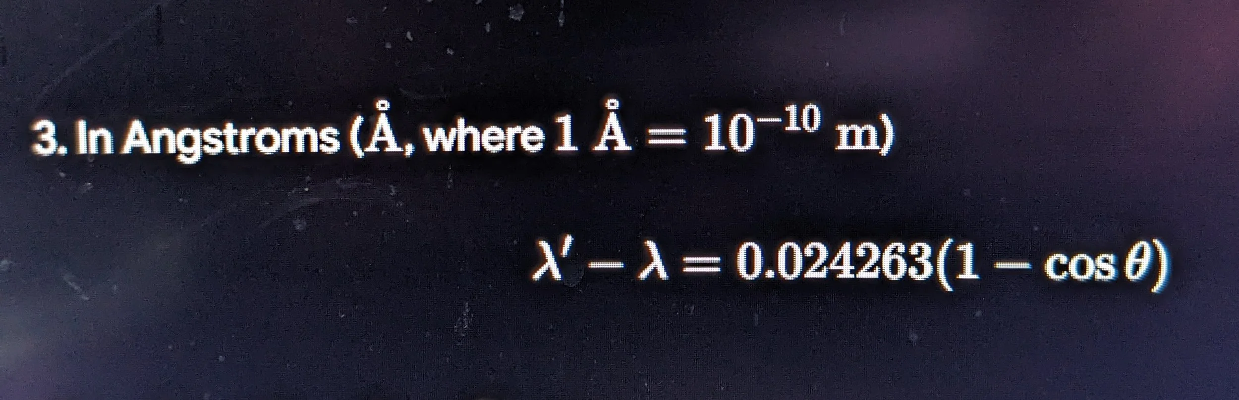 Close-up of a scientific slide or book page showing physics equations related to Angstroms and wavelength. Text includes '3. In Angstroms (Å, where 1 Å = 10⁻¹⁰ m)' and an equation for wavelength change involving cosine of angle.