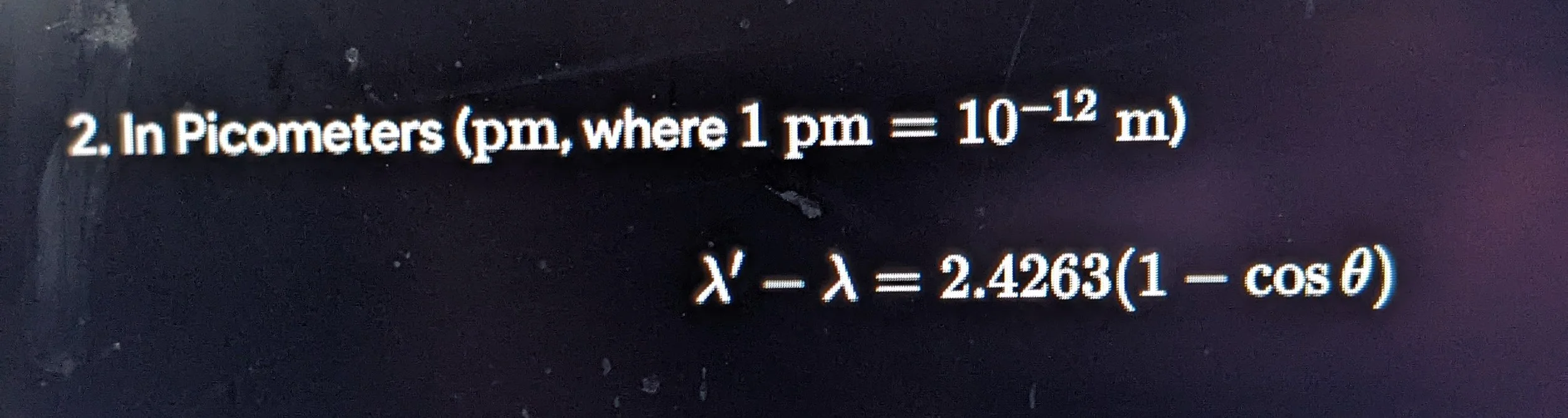 Close-up of a black screen displaying scientific formulas and text related to picometers and wavelength calculations.
