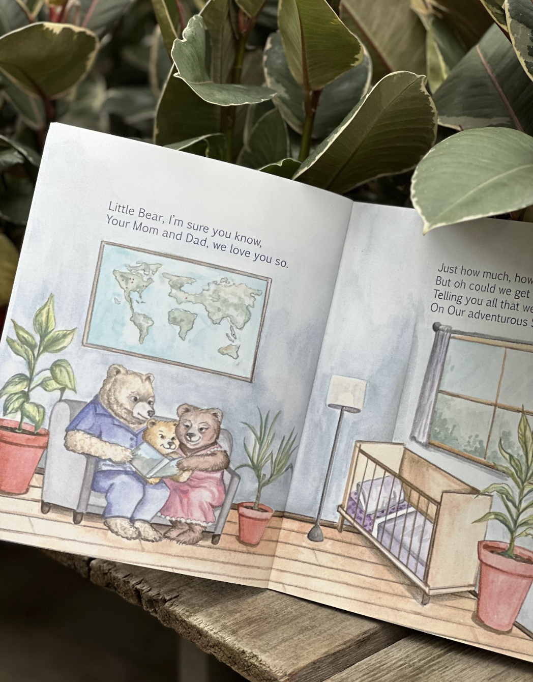 A children's illustrated book showing three bears sitting on a couch, looking at a book, in a cozy room with potted plants, a world map on the wall, and a crib near a window with curtains.