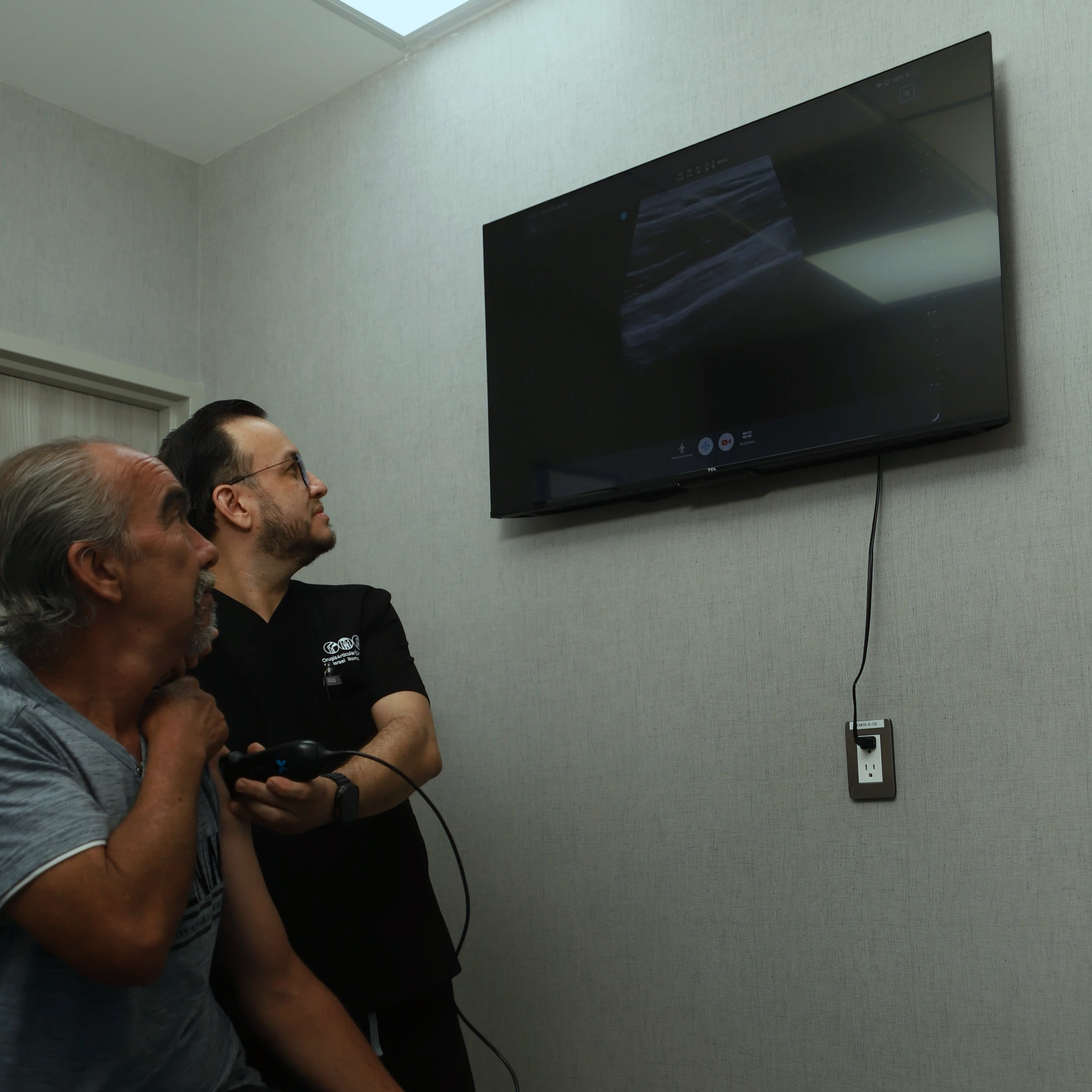 Cuatro personas observando una pantalla de televisión en una sala con paredes de color claro.