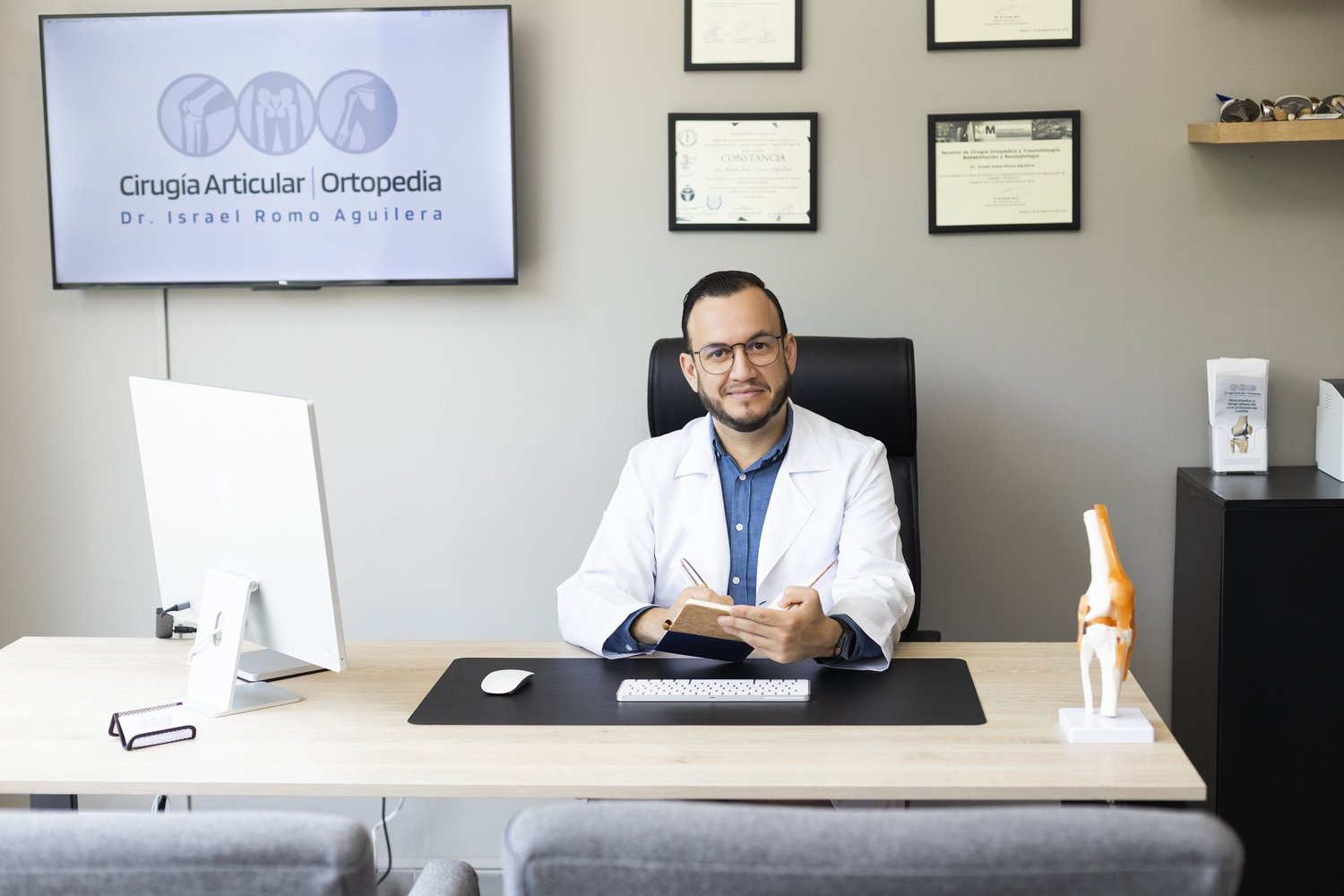Dr. Israel Romo, especialista en rodilla en Guadalajara, en su consultorio con un modelo de rodilla
