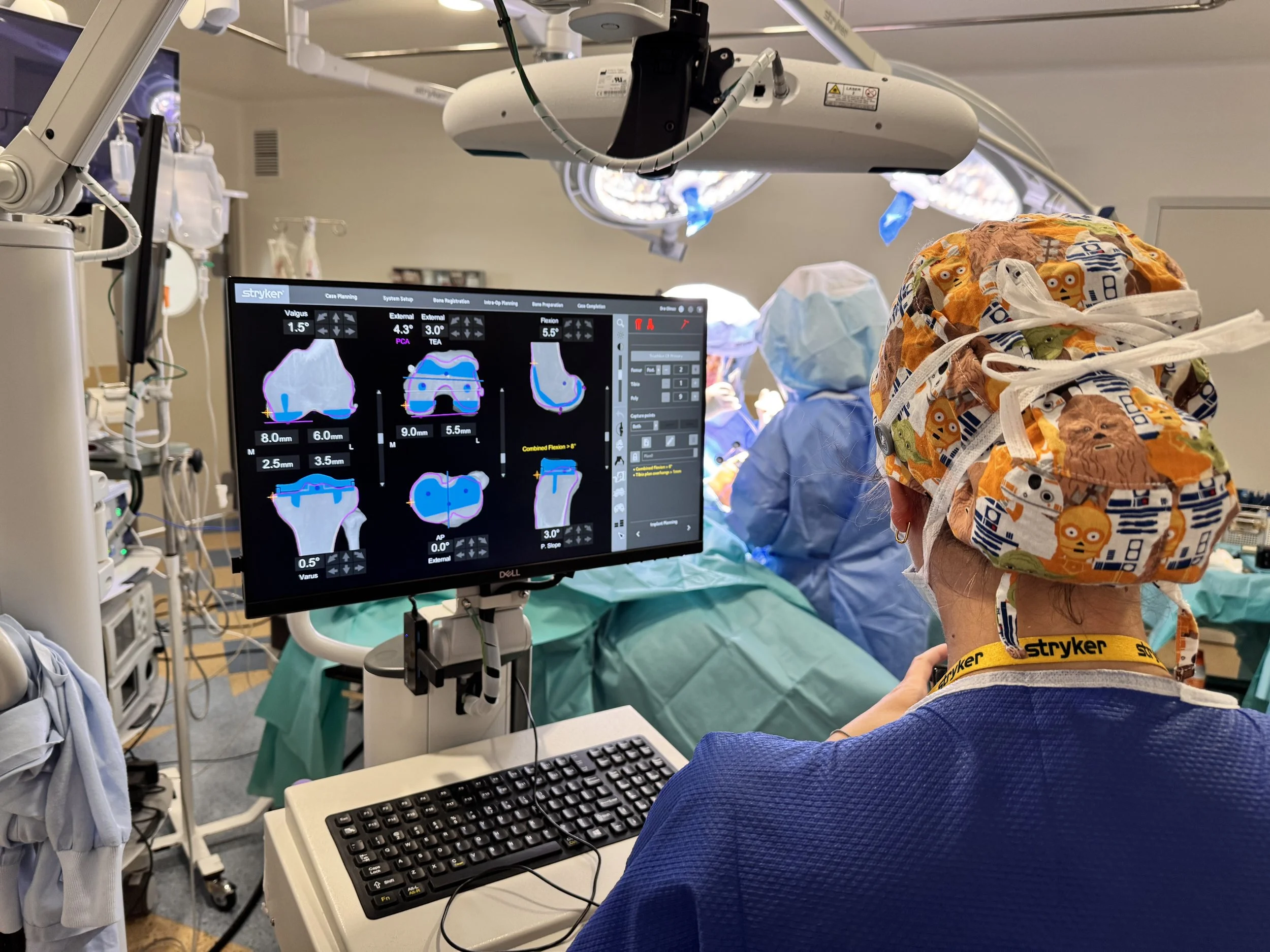 Un quirófano con personal médico operando, monitoreando datos en una pantalla, mientras una paciente está en cirugía. Cirugia robótica de rodilla