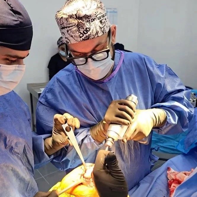 Equipen médico del Dr. Israel Romo realizando una cirugía en un paciente, colocando una prótesis de rodilla e instrumentos en un entorno hospitalario.