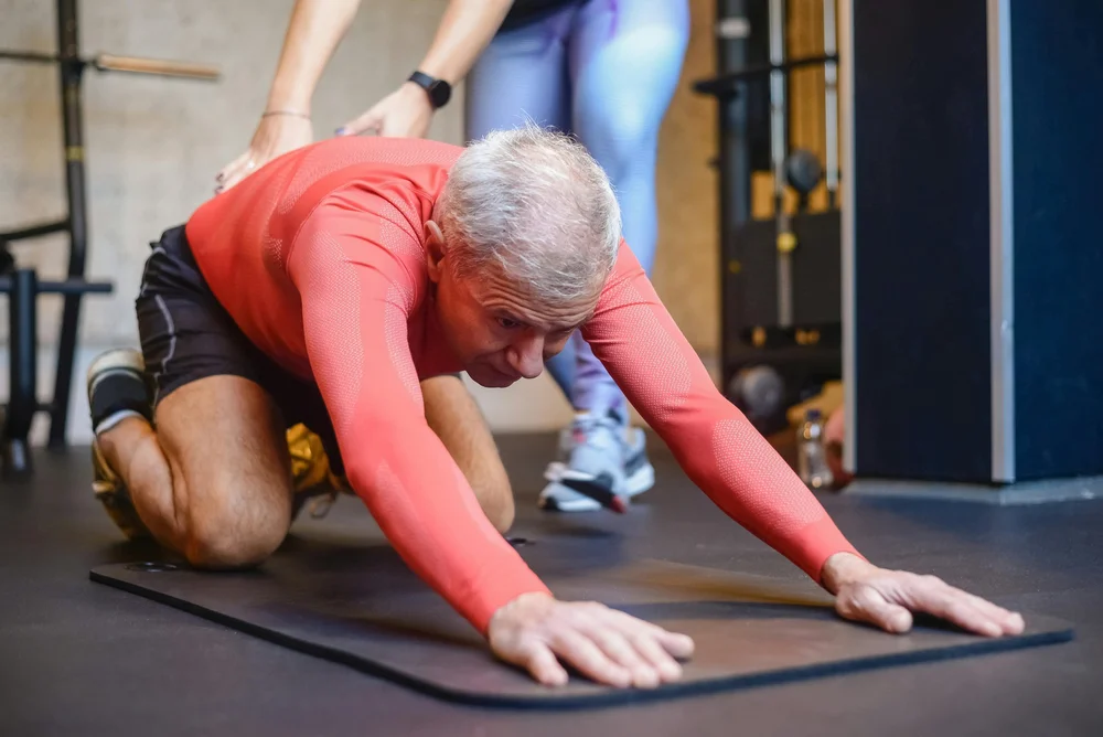 Adulto mayor hace ejercicios de rehabilitación con apoyo de un terapeuta