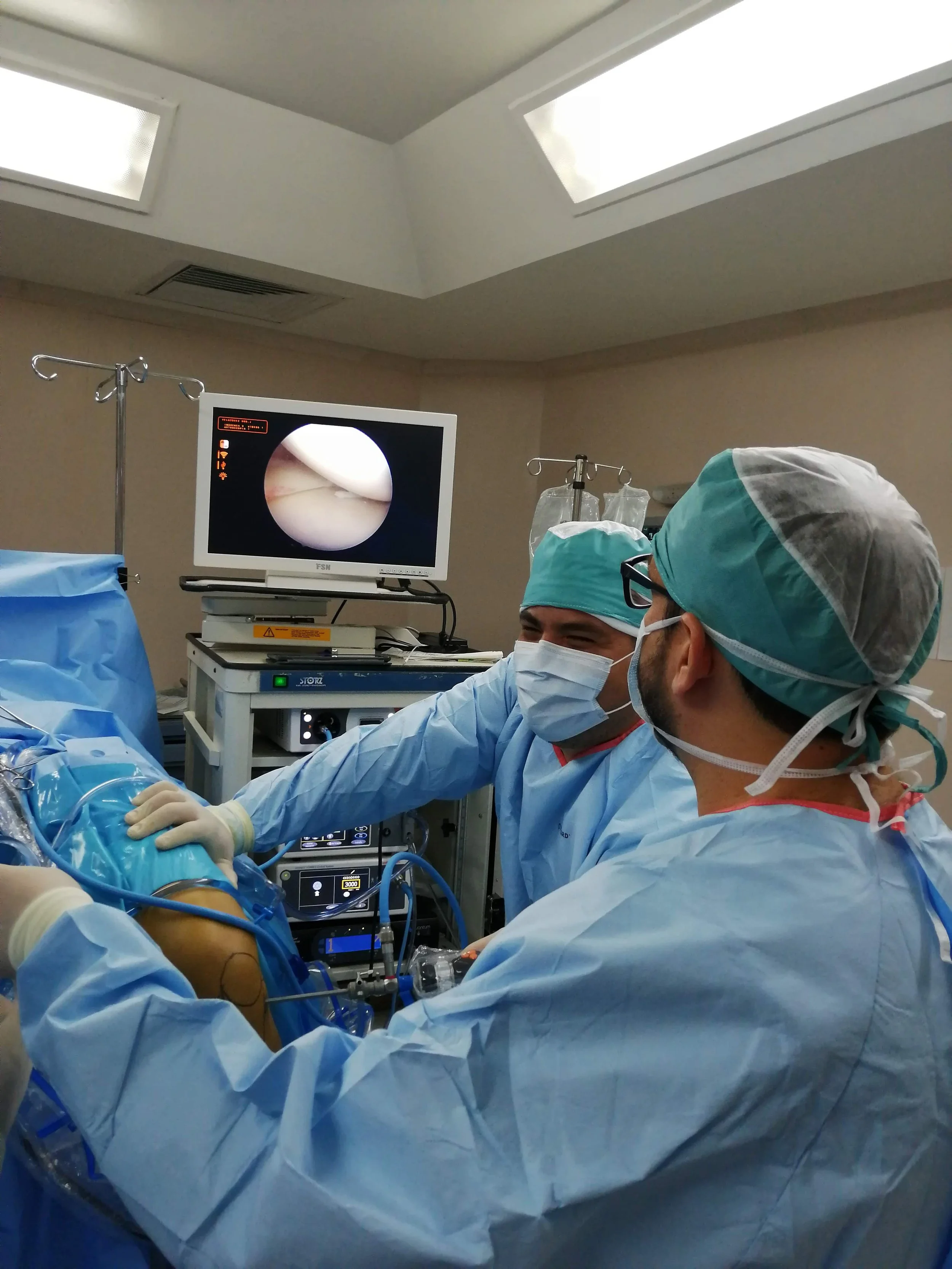 Personal médico realizando una cirugía en un quirófano, con un monitor que muestra una vista interna del cuerpo y equipo médico a su alrededor.