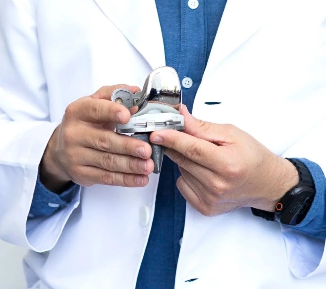 Persona con bata blanca y reloj, usando un dispositivo medidor de presión arterial en la mano mientras sostiene un estetoscopio.