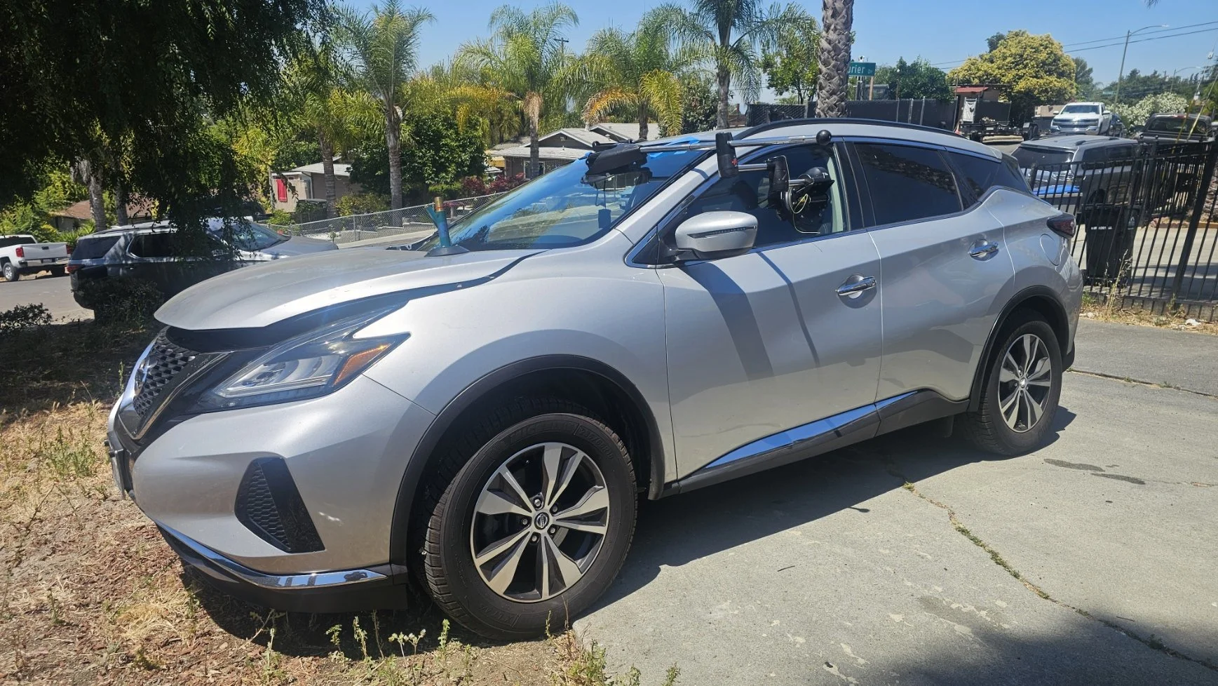 Silver SUV parked on a driveway with palm trees and houses in the background.