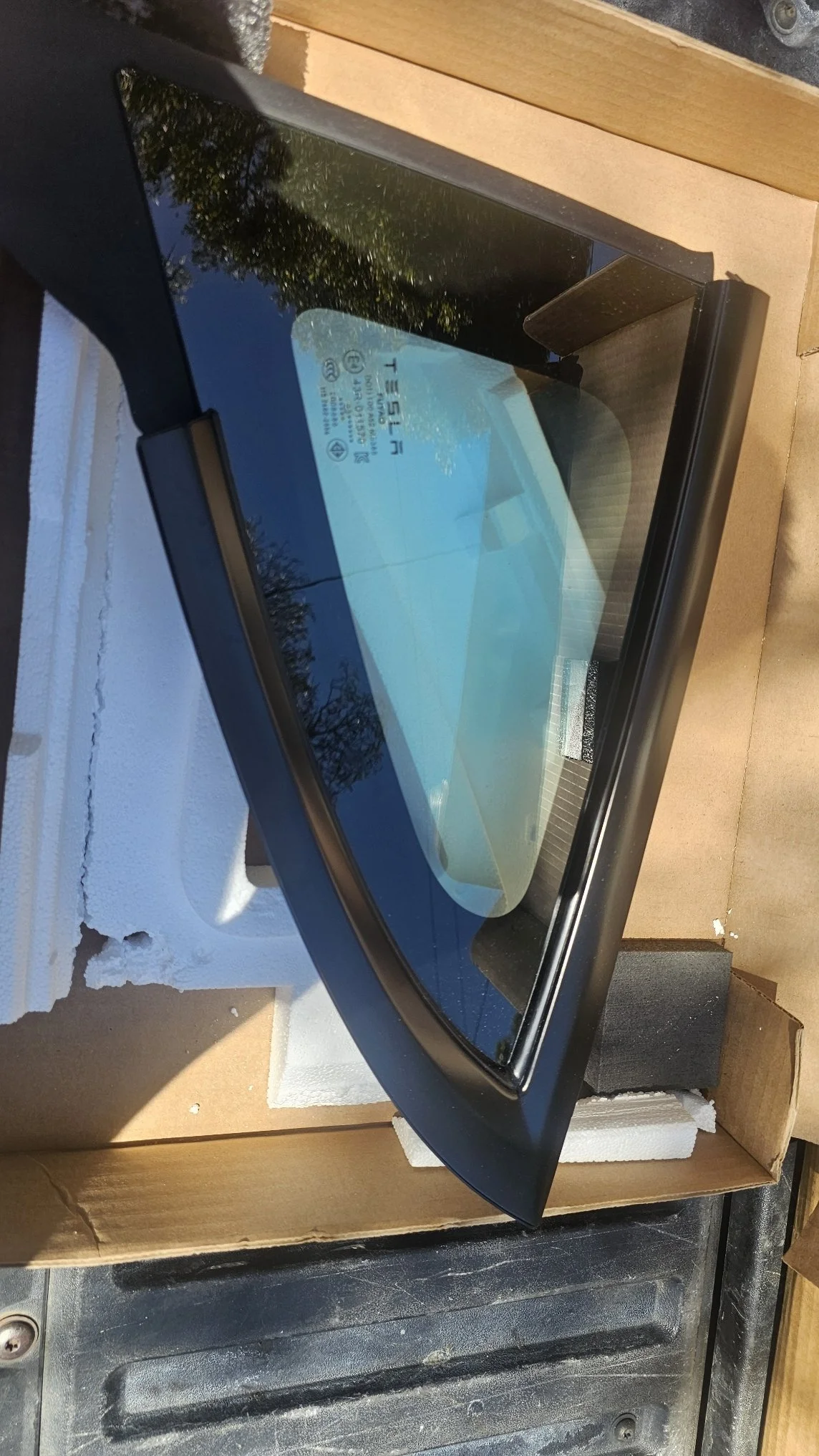A car rearview mirror with a blue tint, mounted on a car's interior, resting inside a cardboard box with foam padding around it.