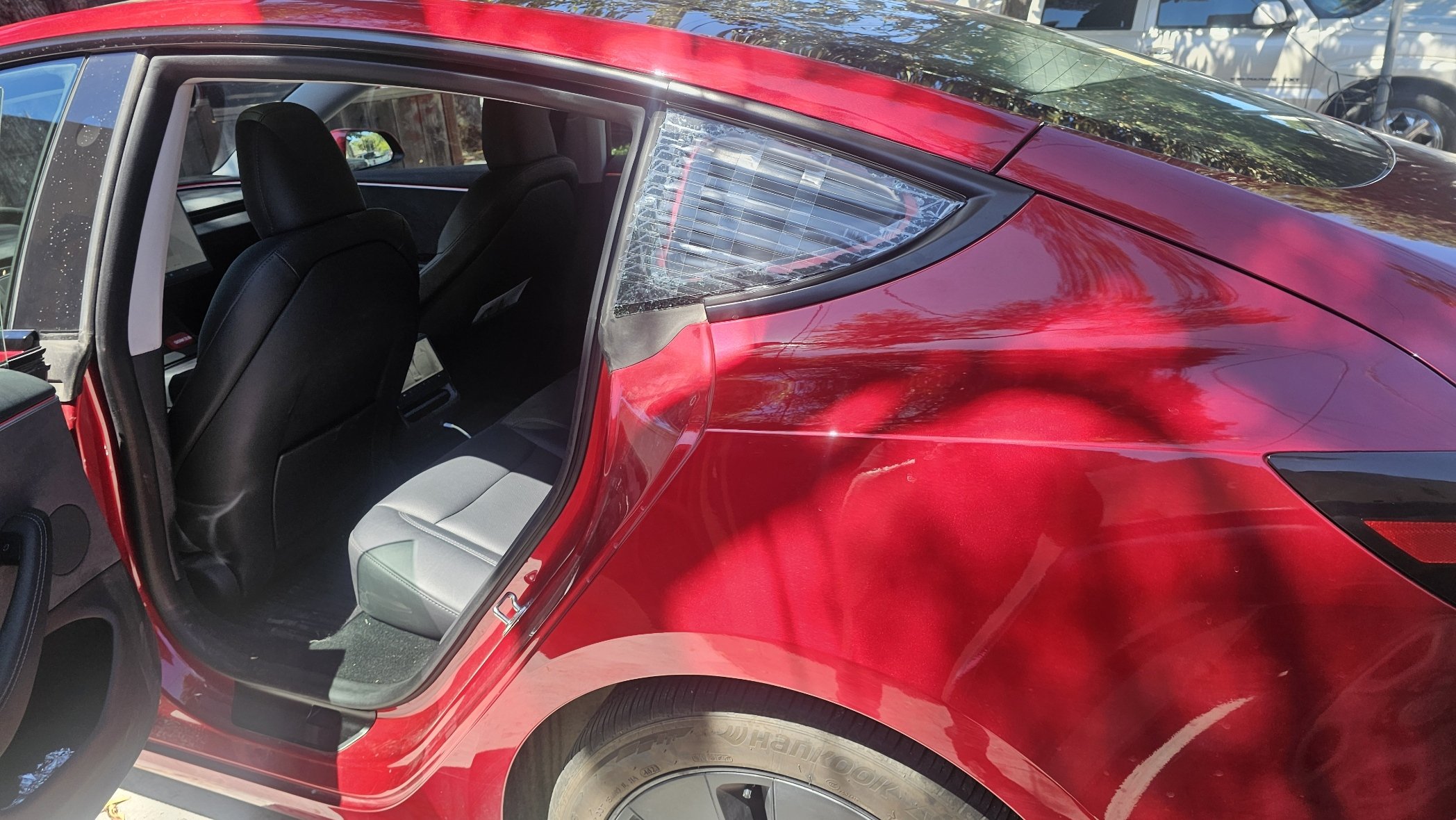 Red car with an open rear door showing black and gray interior seats and cracked rear side window