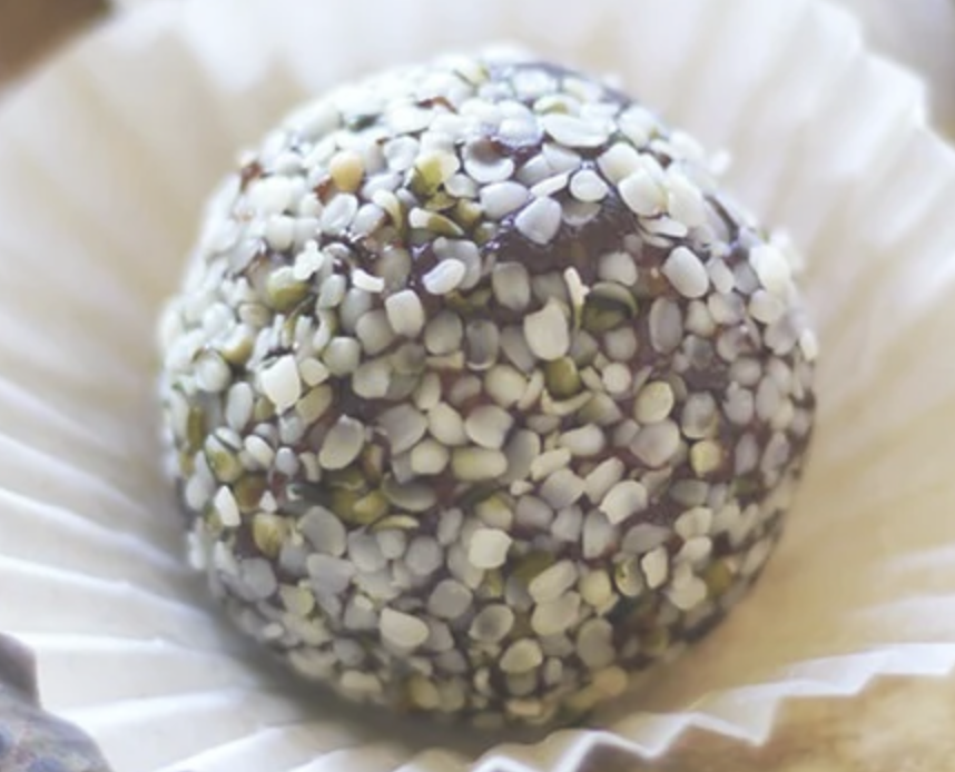 A chocolate truffle coated with white and green chopped nuts, resting on a paper cupcake liner.