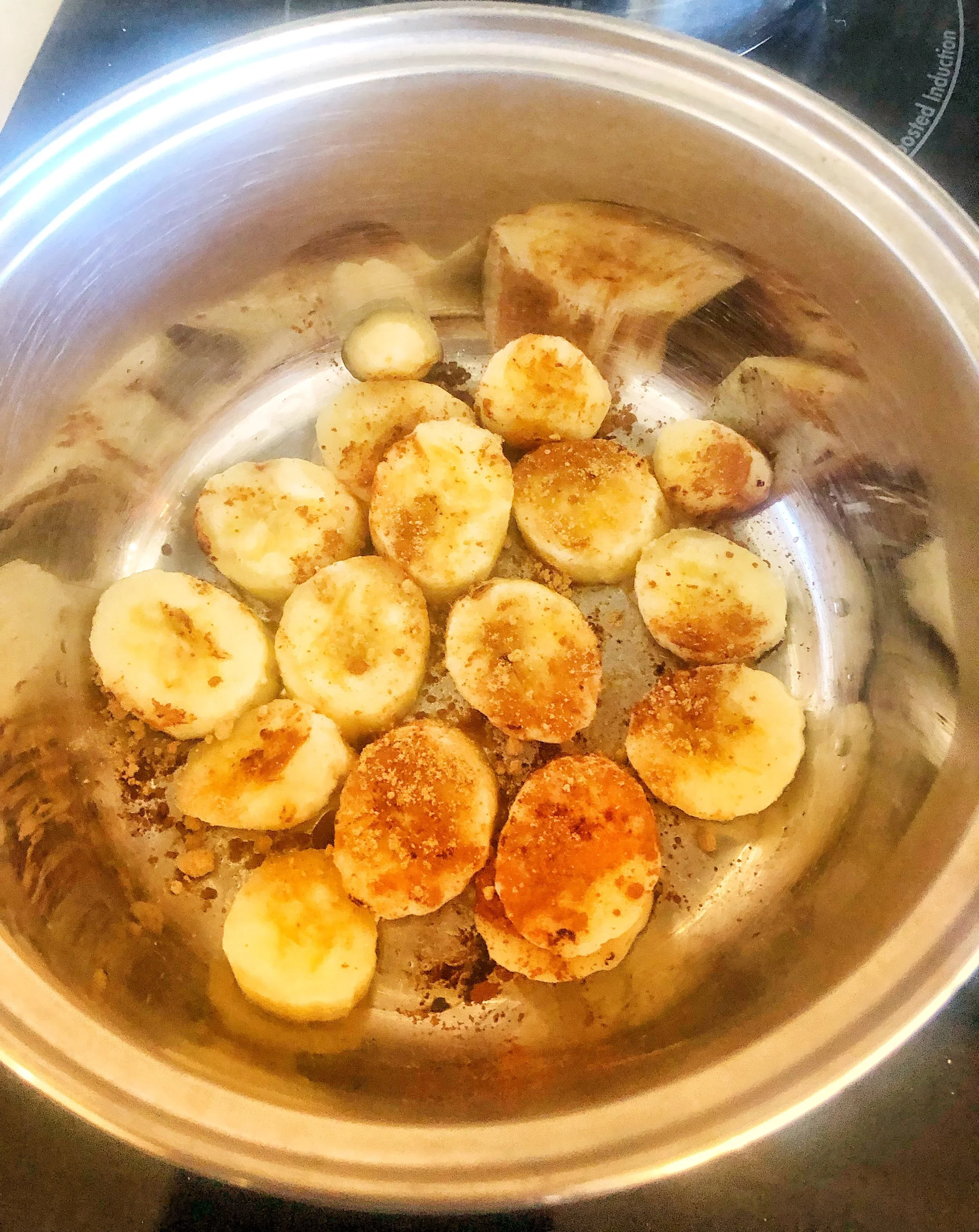 Slices of bananas being cooked with cinnamon and brown sugar in a stainless steel pot.