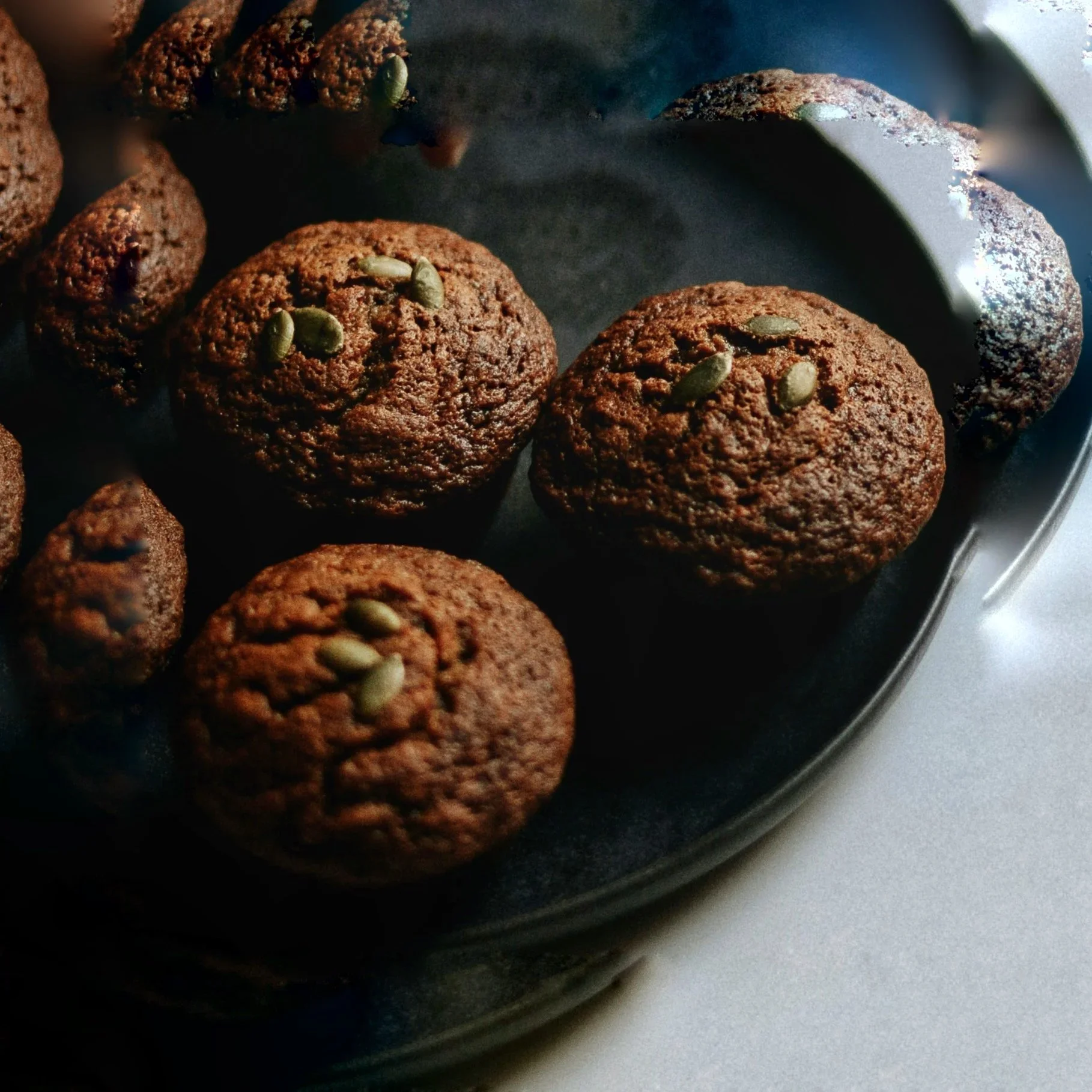 Close-up of freshly baked chocolate cookies with pumpkin seeds on top, placed in a metal tray.