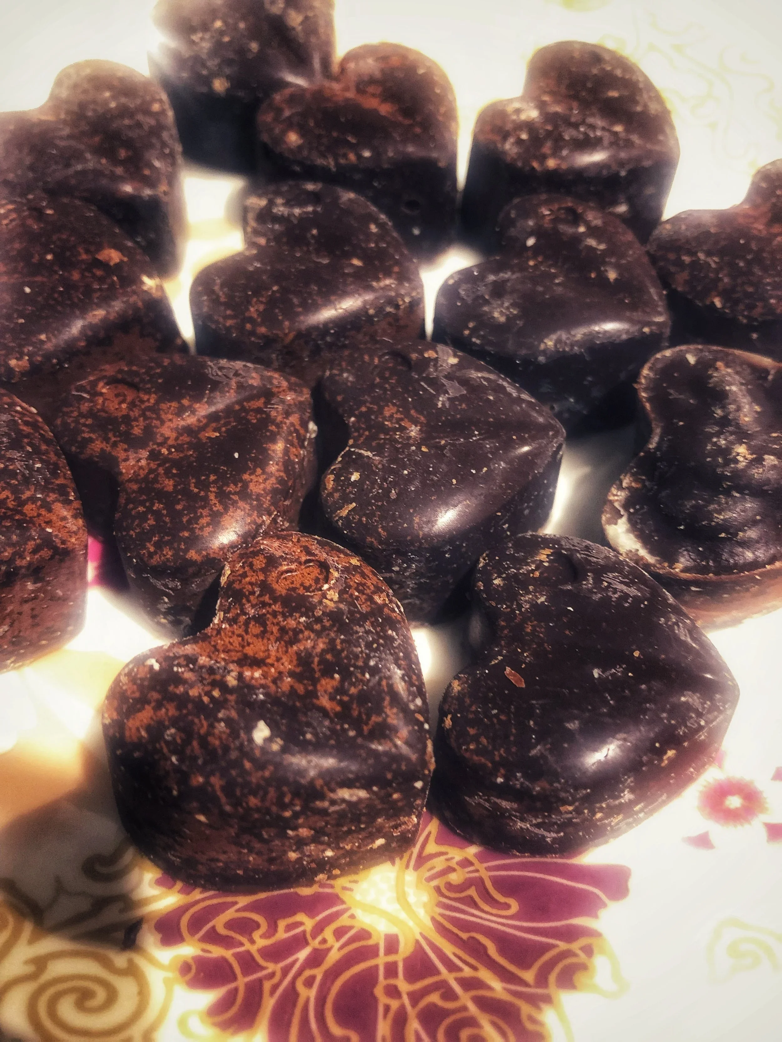 Close-up of several dark brown heart-shaped candies with a textured surface on decorative paper.
