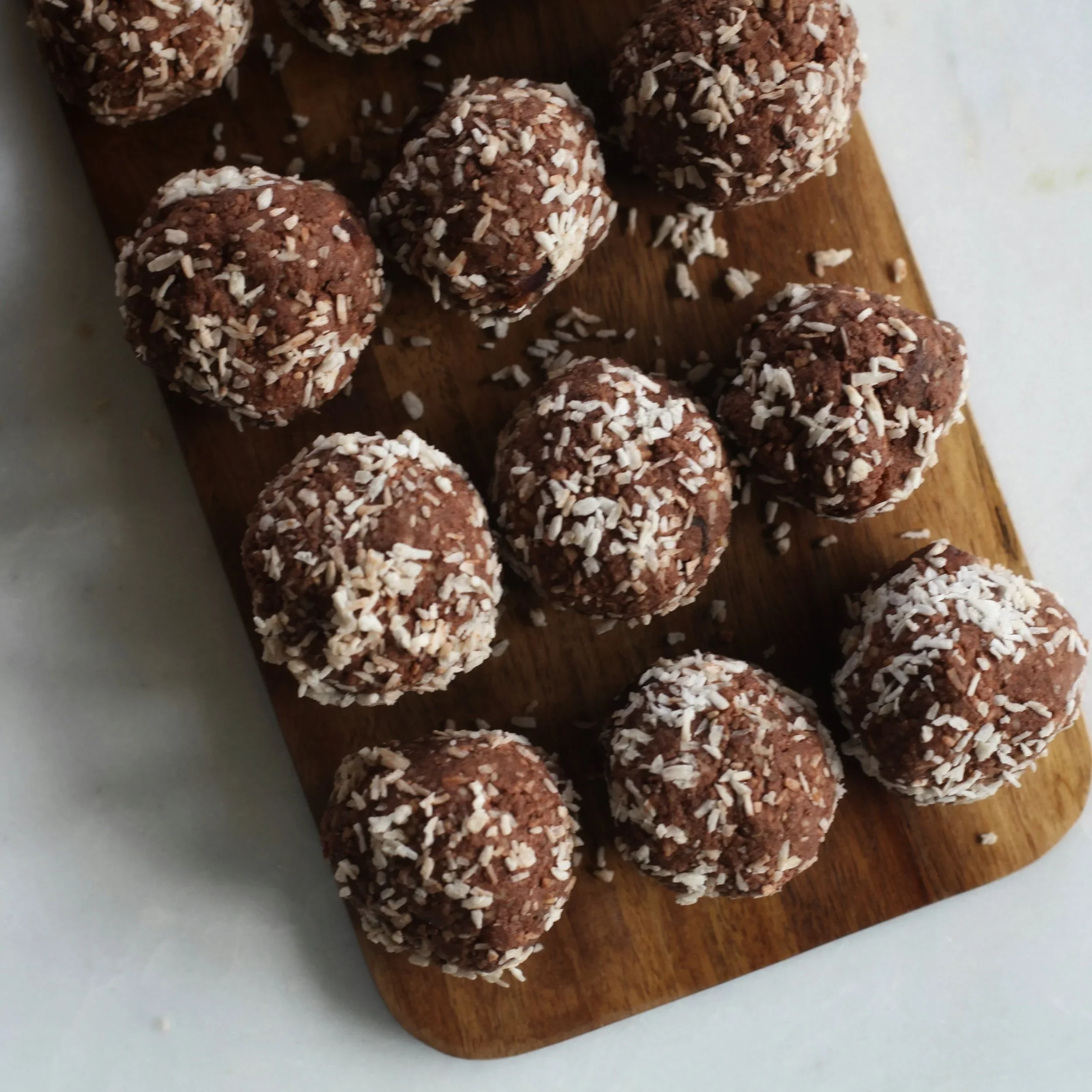 Chocolate truffles covered with shredded coconut resting on a wooden cutting board.