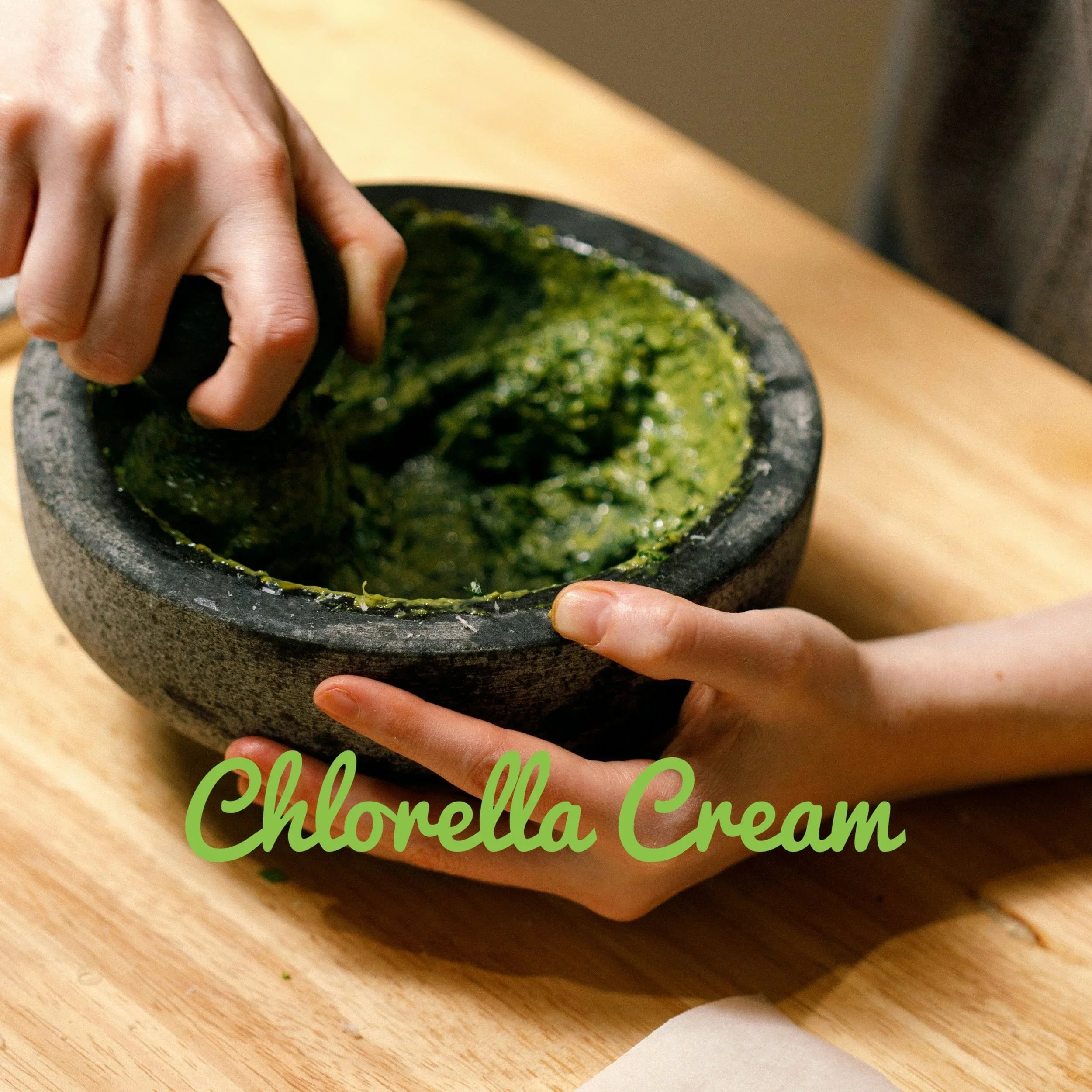 Close-up of a person holding a black stone mortar and pestle, grinding green ingredients, Homemade Chorella Cream.