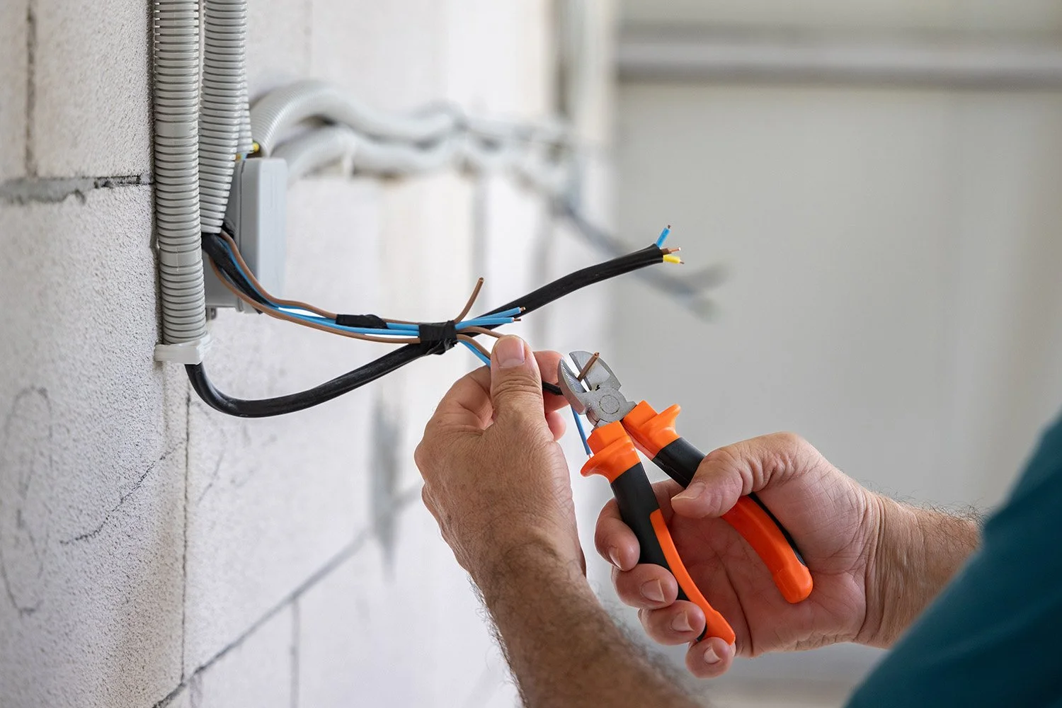 A person using wire cutters to cut an electrical wire in a wall outlet box.