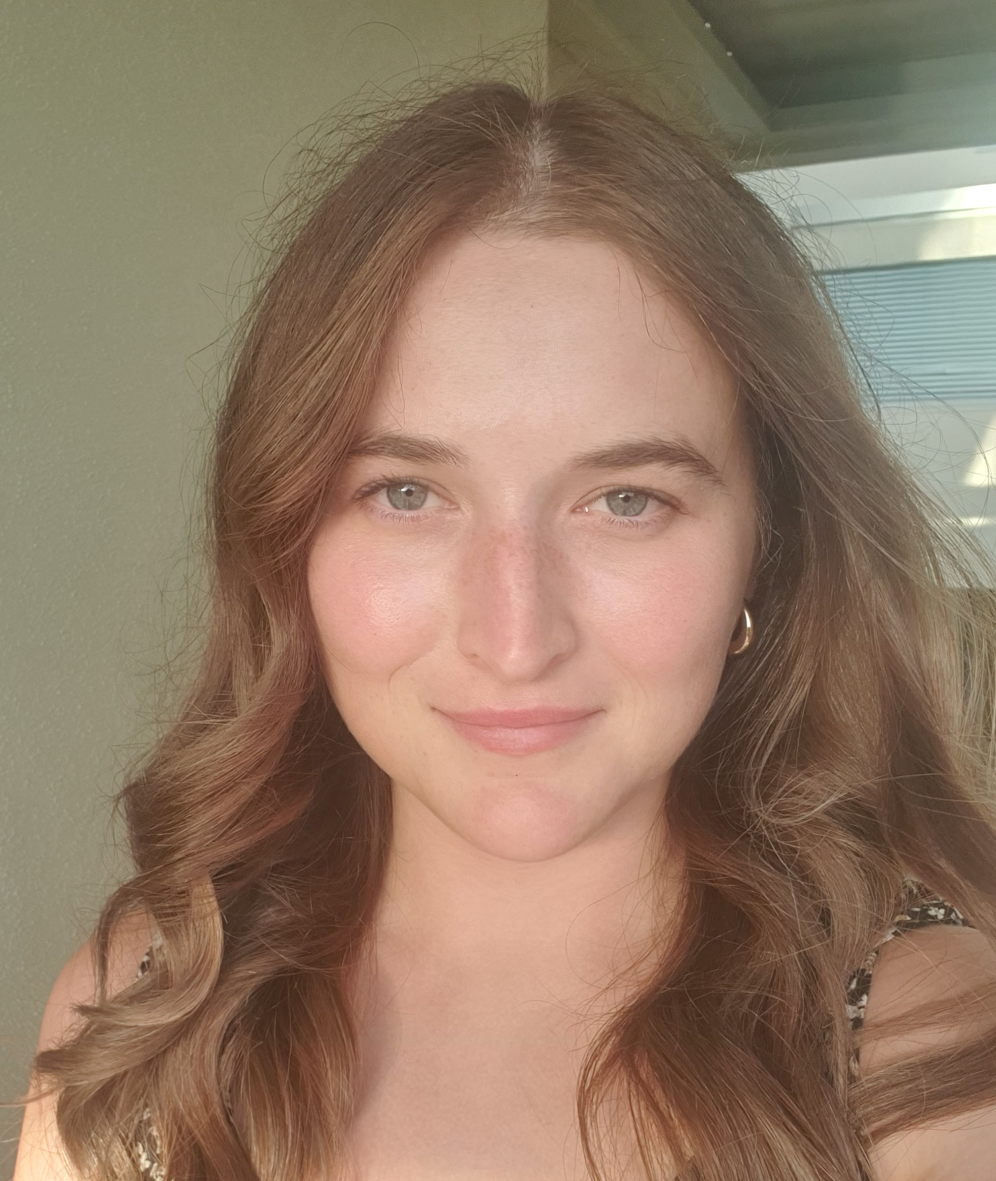Close-up of a young woman with wavy brown hair, light makeup, and wearing a sleeveless top with a leopard print pattern.