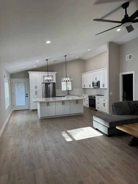 Open-concept kitchen with white cabinets, stainless steel appliances, a large island, pendant lighting, and a gray sofa in the living area.
