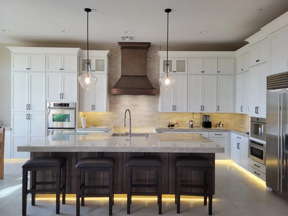 Modern kitchen with white cabinets, a large island with dark stools, stainless steel appliances, and pendant lights over the island.