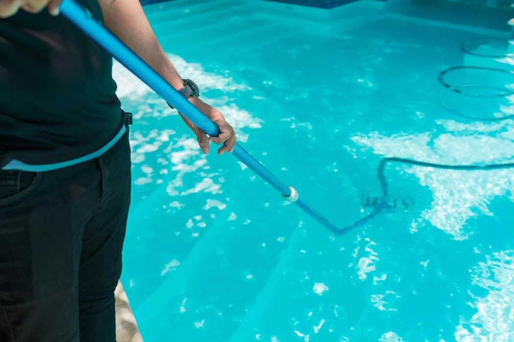 Person cleaning a swimming pool with a long-handled brush.