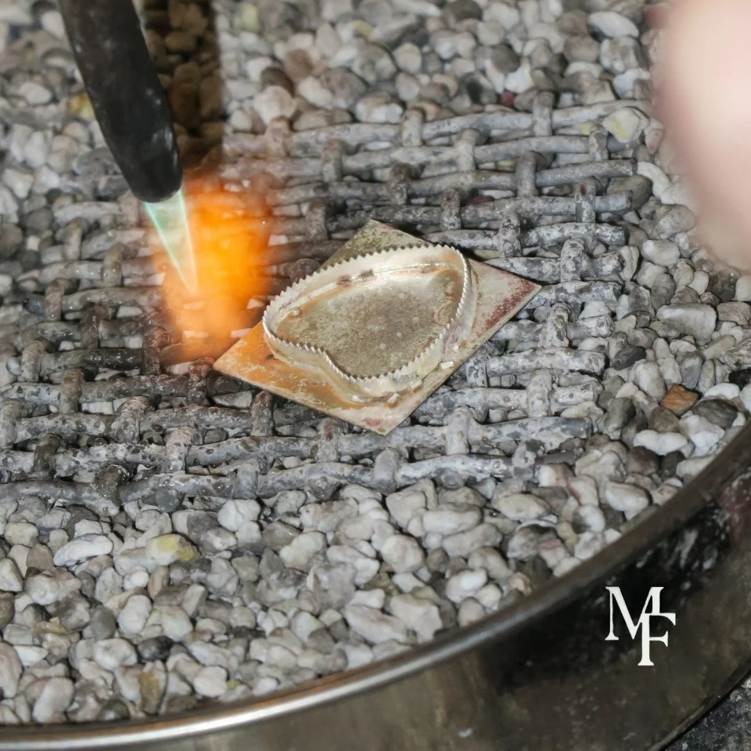 A close-up of a piece of metal being welded using a torch, with a bed of small gray and white rocks underneath.