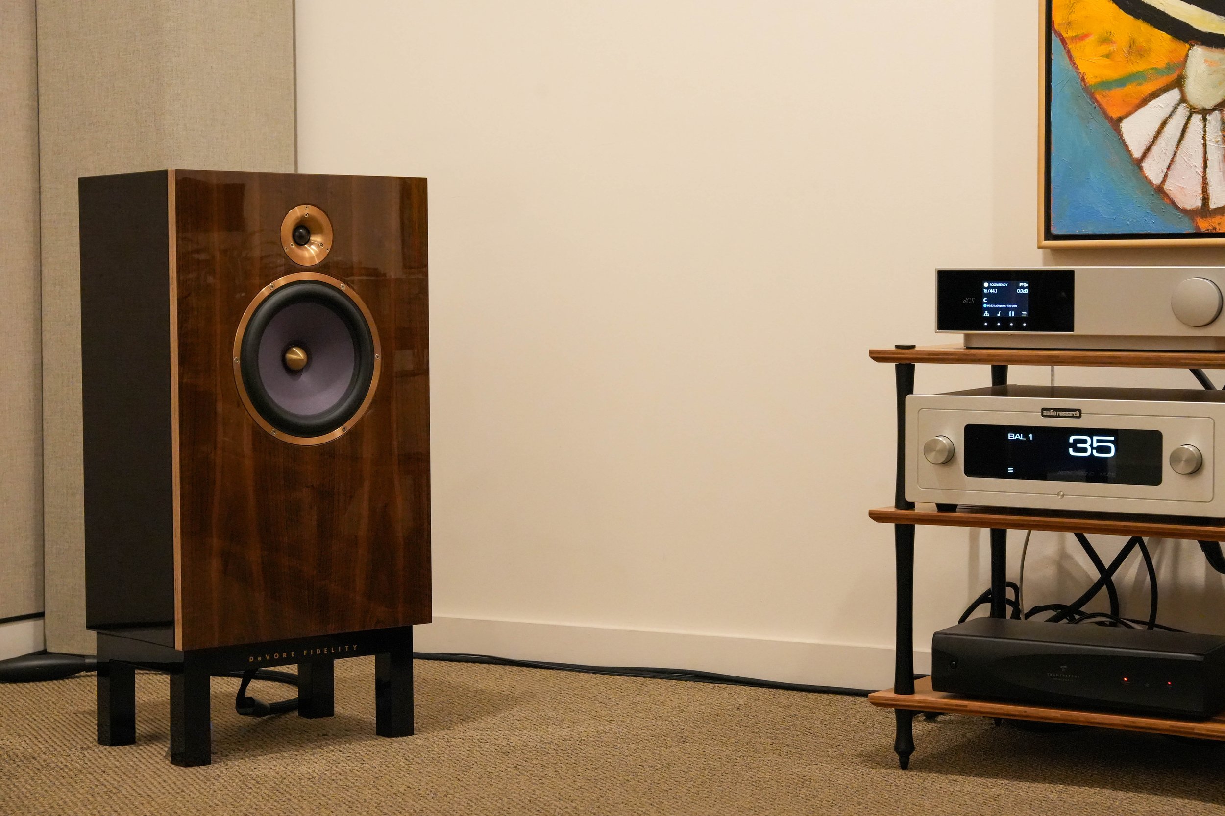 High-end audio equipment including a large wooden speaker and audio receiver on a black and wooden stand.