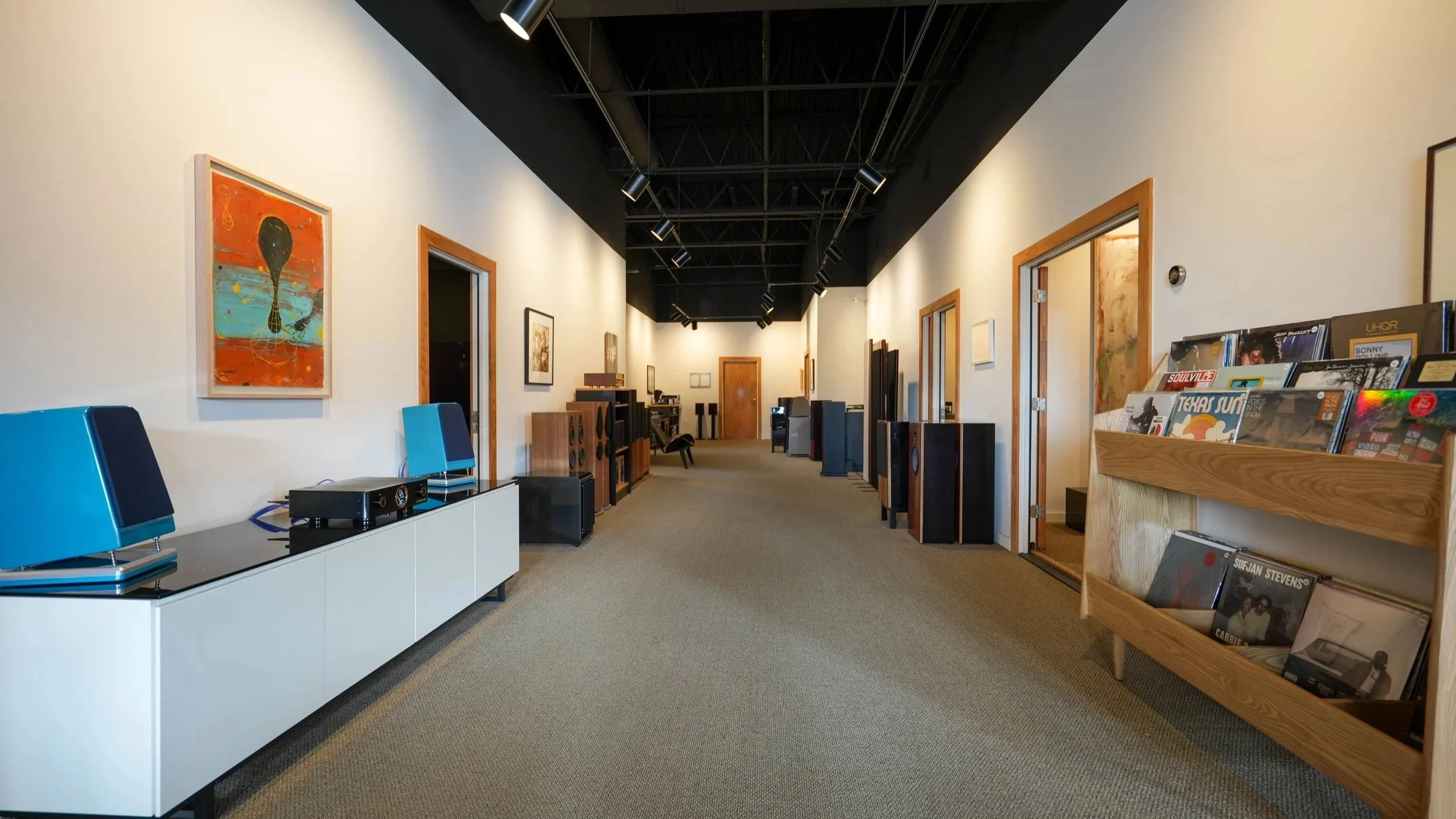 Artwork on the left wall, record collection on the right, and audio equipment on a white cabinet, in an art gallery or music store interior.